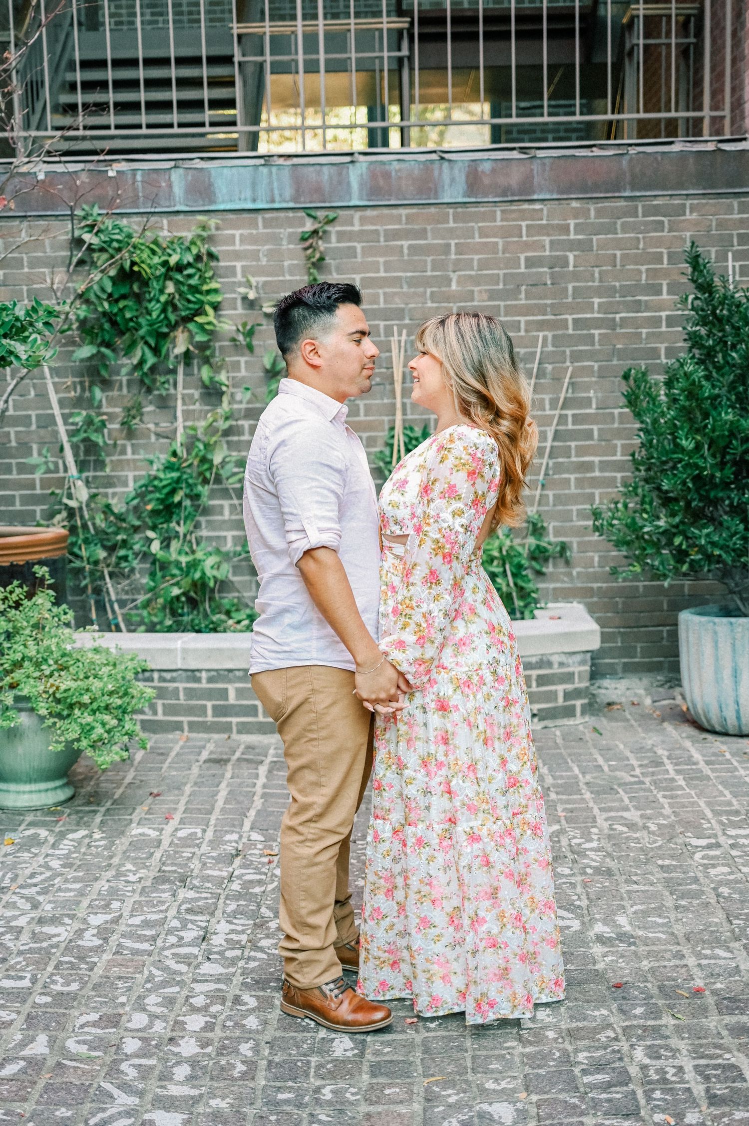 Couple holding hands and gazing at each other in a charming courtyard setting.