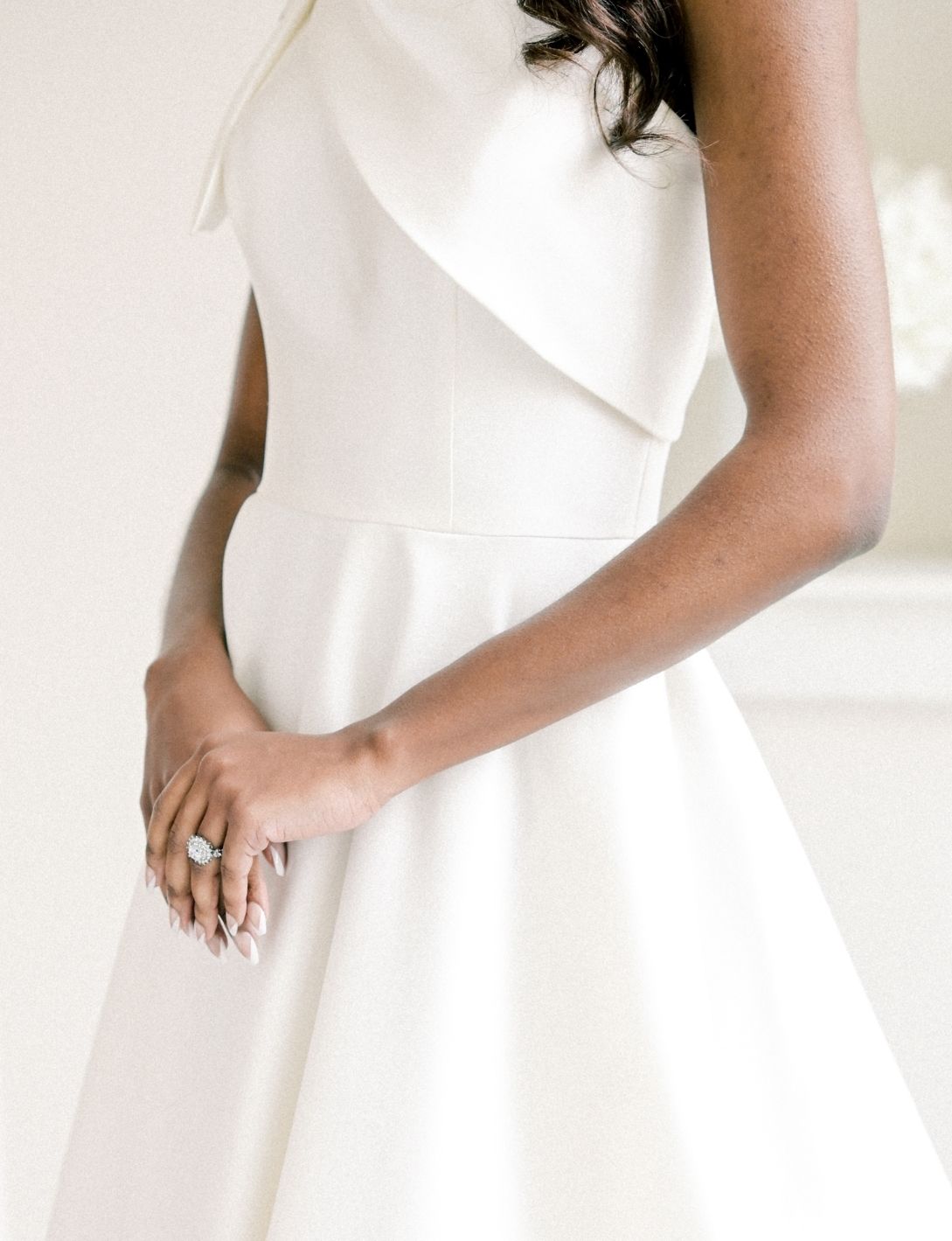 Elegant bride in a white sleeveless wedding dress with ruffle detail, showcasing a sparkling engagement ring.