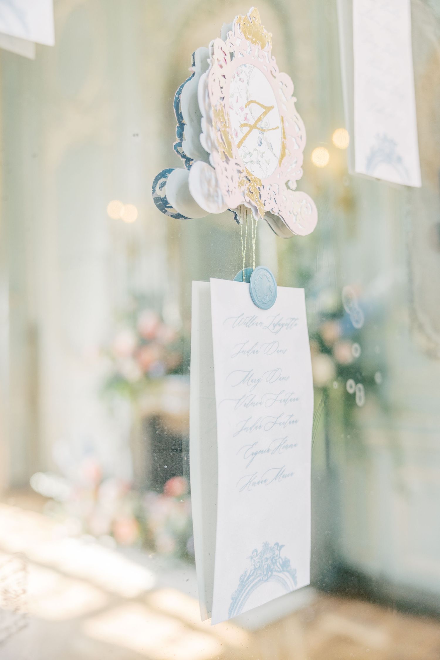 Elegant wedding program displayed in a white gift bag with decorative crest topper in soft blue and gold tones.