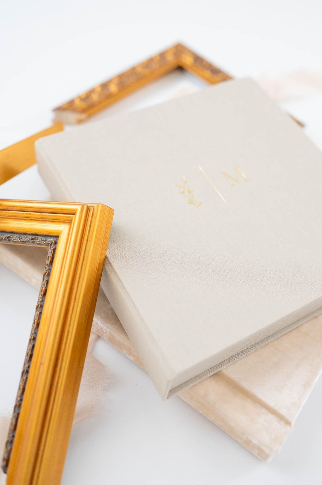 Gold ornate picture frames leaning against cream linen wedding albums with monogram embossing on white background.