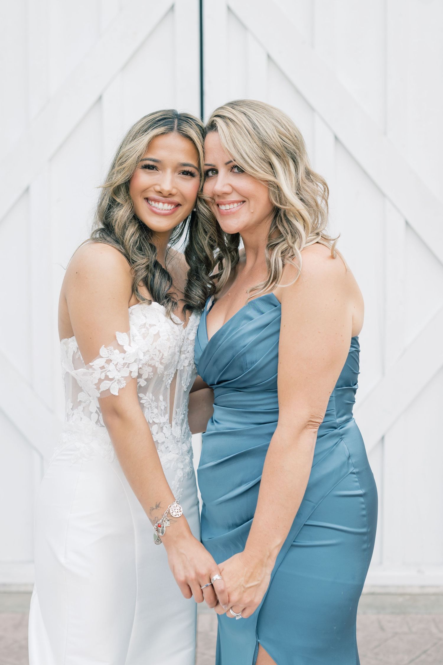 Bride in lace gown and bridesmaid in blue satin dress smiling together before white barn doors.
