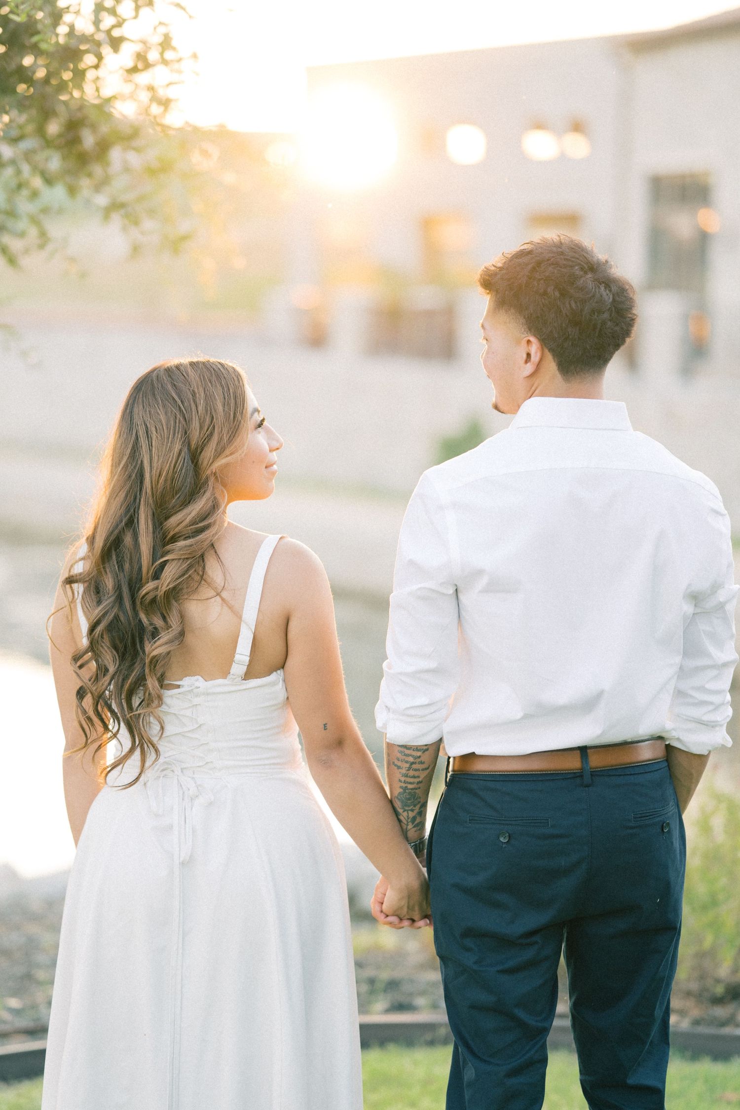 Couple holding hands walking toward a stunning sunset, woman in white dress with flowing hair.