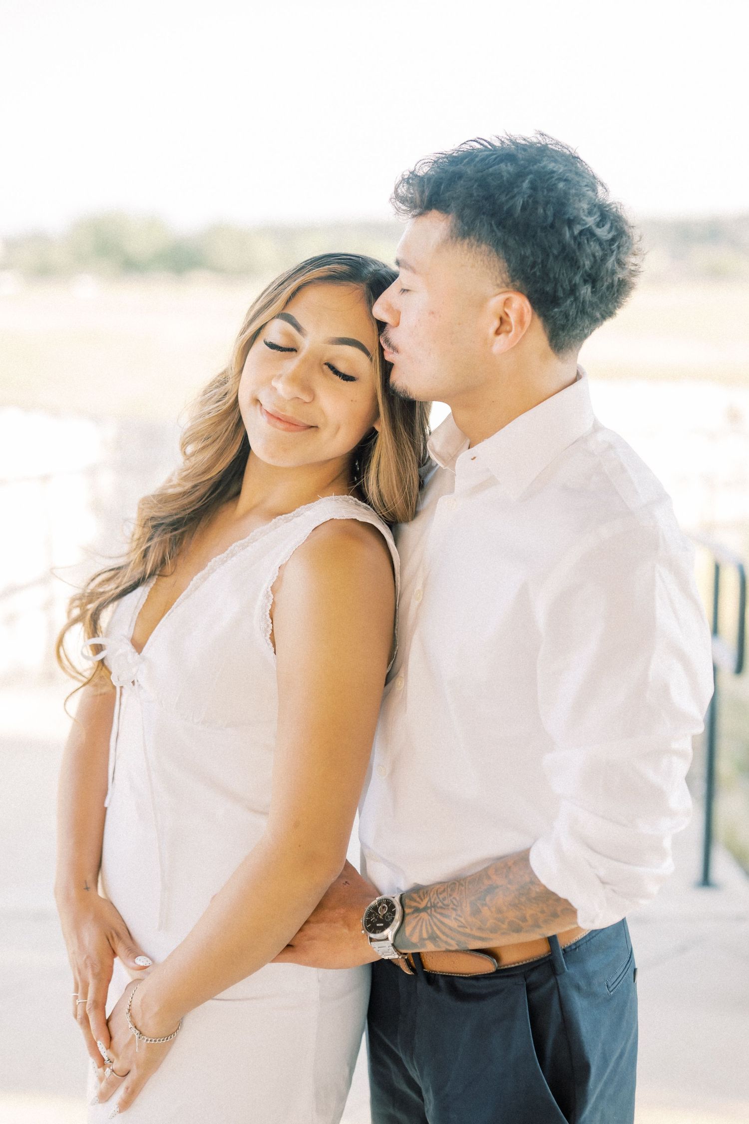 A couple shares a tender moment as the man gently kisses the womans cheek while she smiles softly.