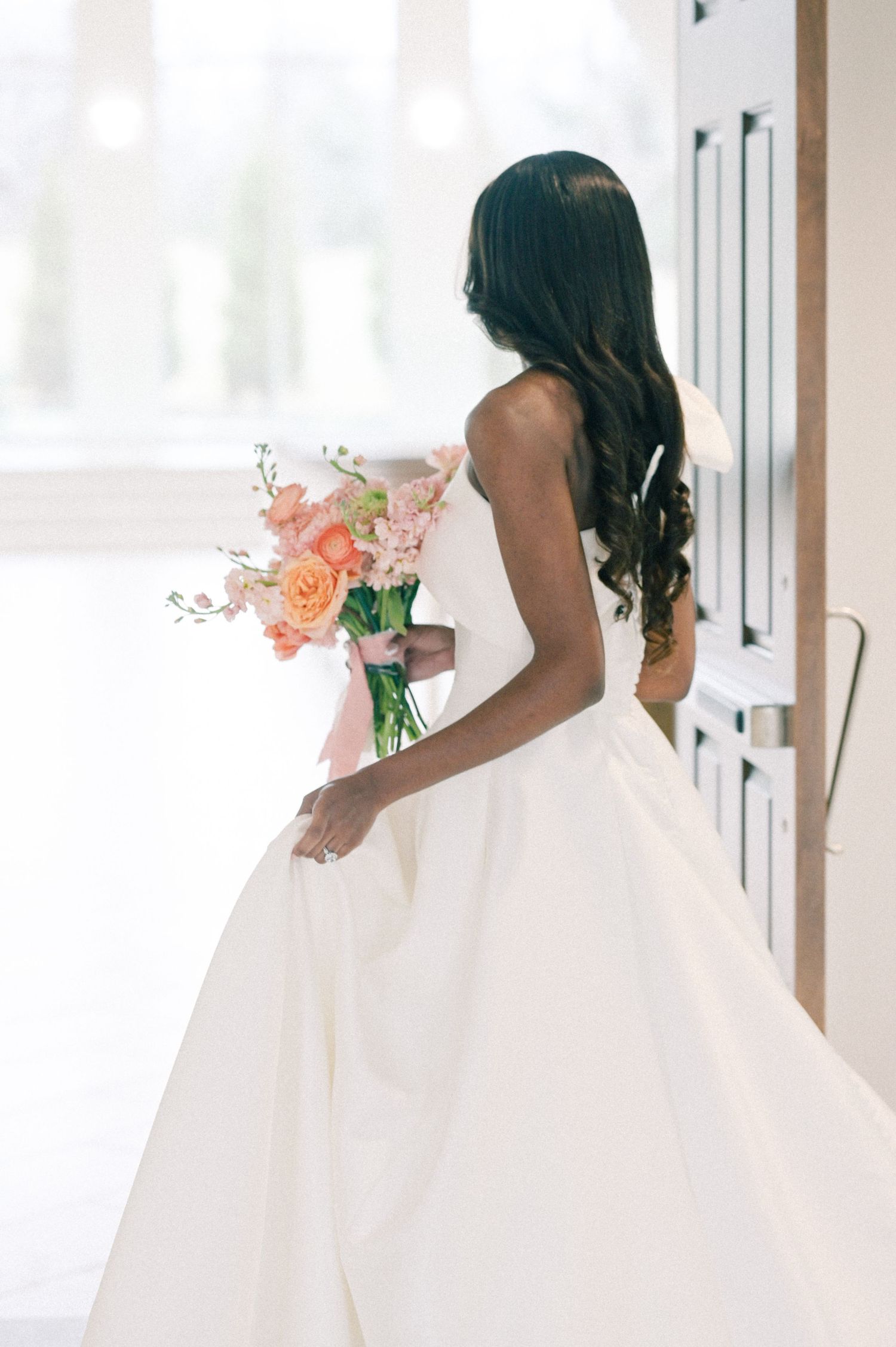 Side view of bride in flowing white gown holding coral and peach floral bouquet.