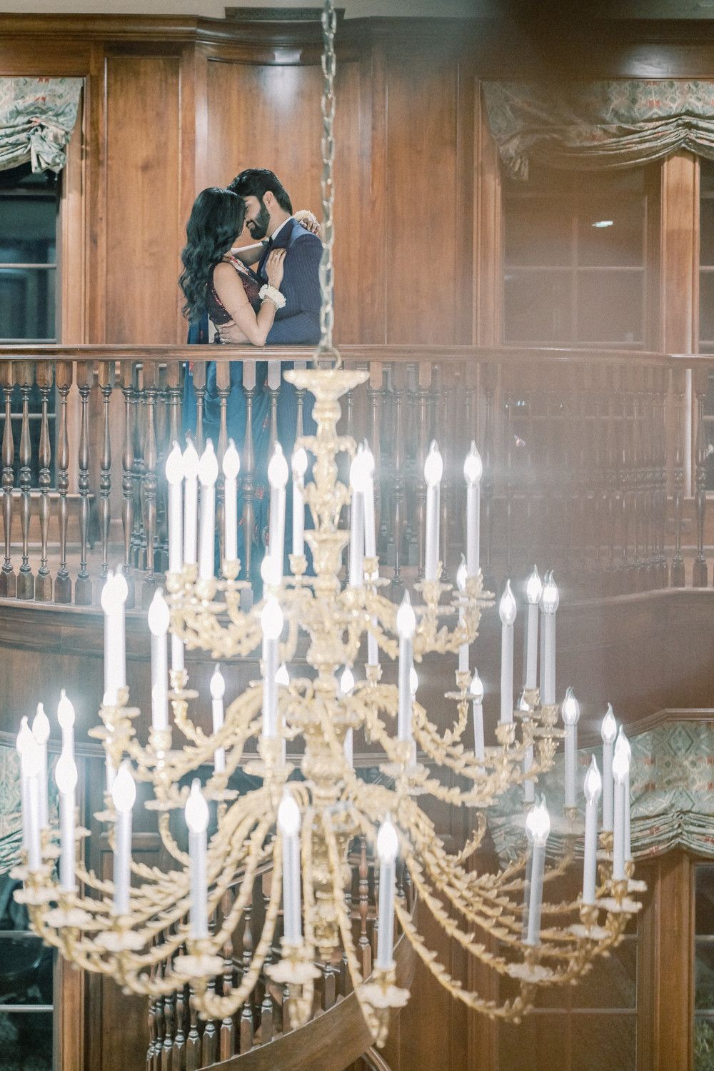 Elegant crystal chandelier frames couple on vintage wooden balcony.