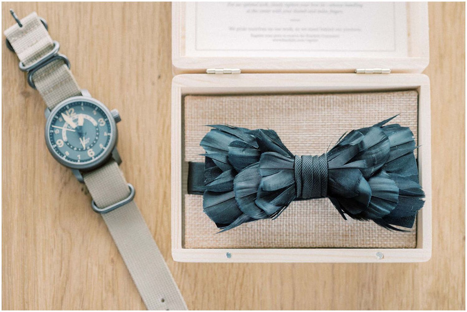 Classic navy blue bow tie and silver watch displayed on a light wooden surface.