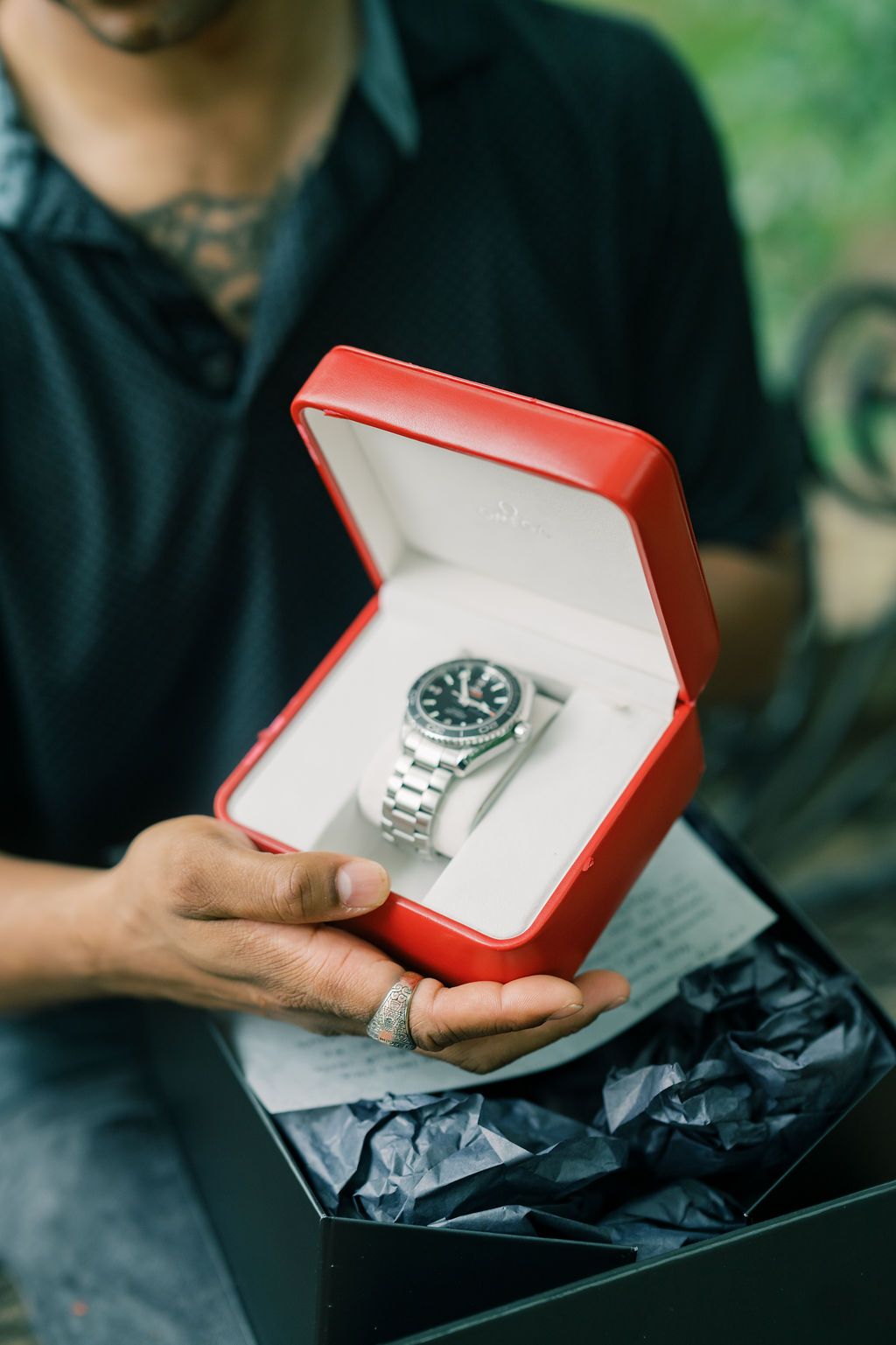 Man holding open red gift box displaying a luxury silver watch with black dial, perfect for special occasions.