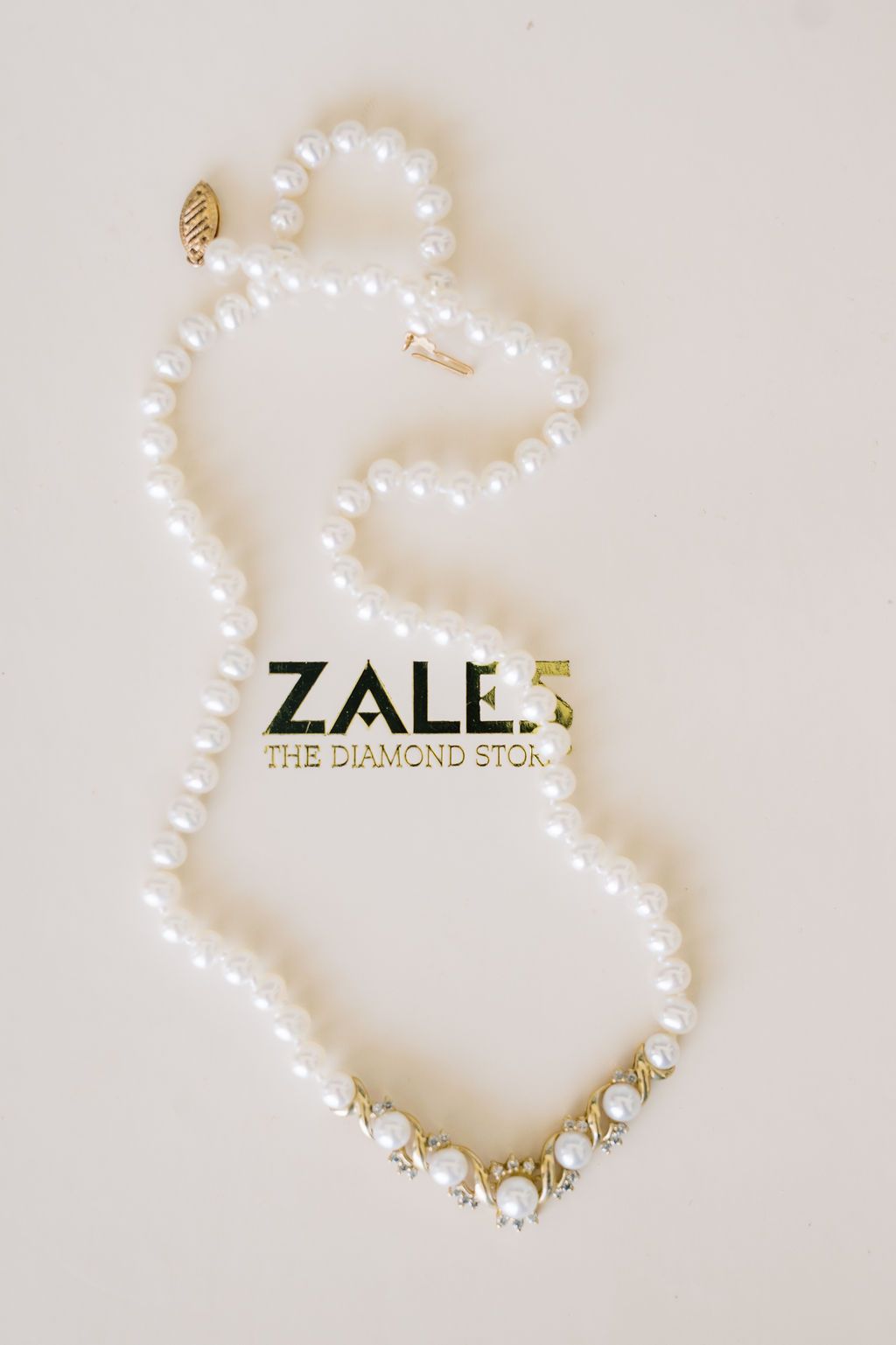 Zales pearl and diamond necklace with gold clasp arranged elegantly on a cream background.