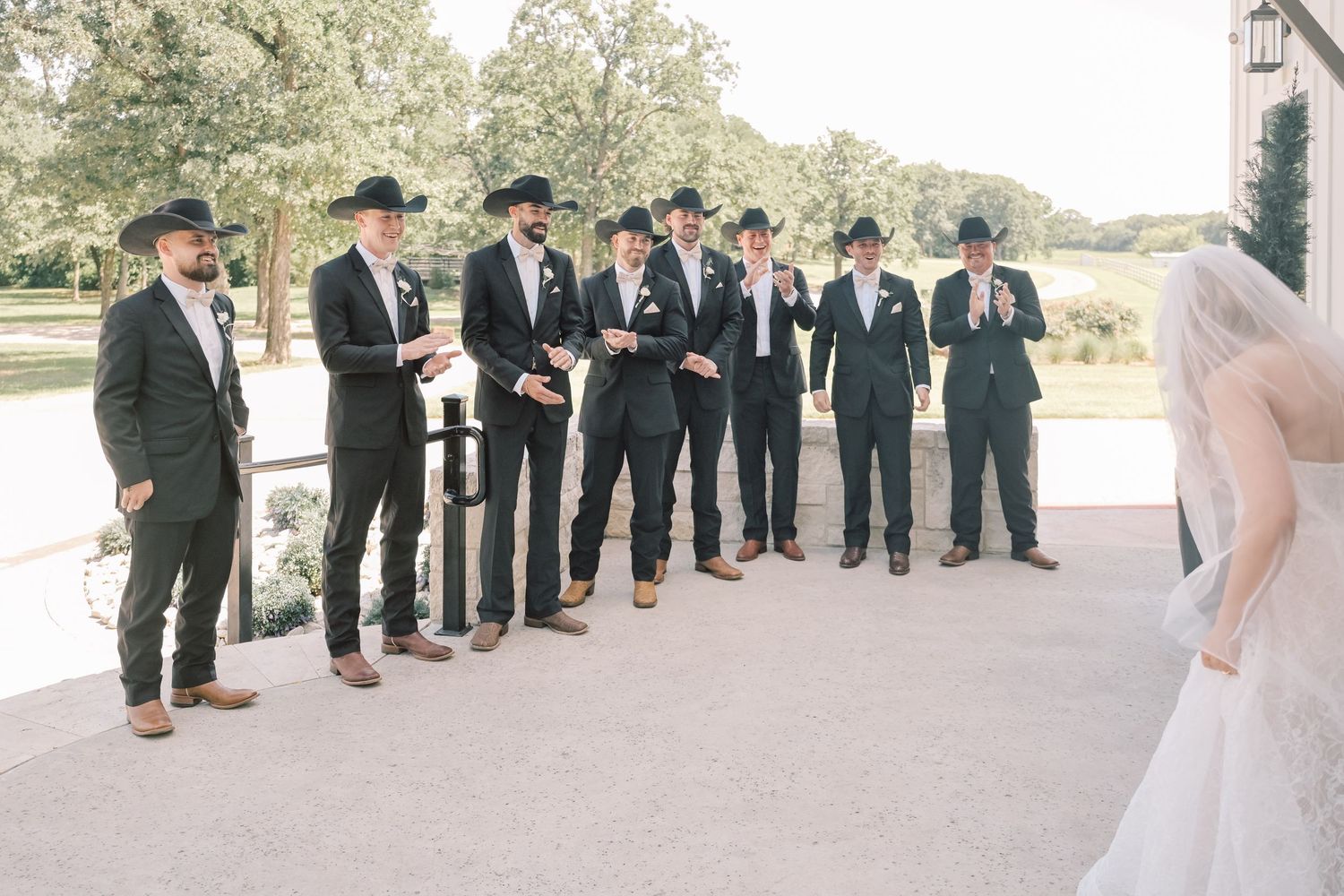 Groomsmen in dark suits and cowboy hats react with excitement as bride approaches for first look reveal.