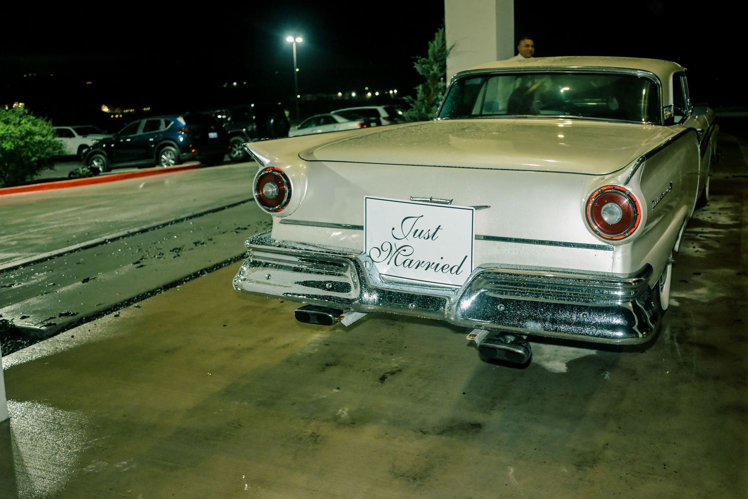 Vintage white Ford car with Just Married sign parked at night after wedding.