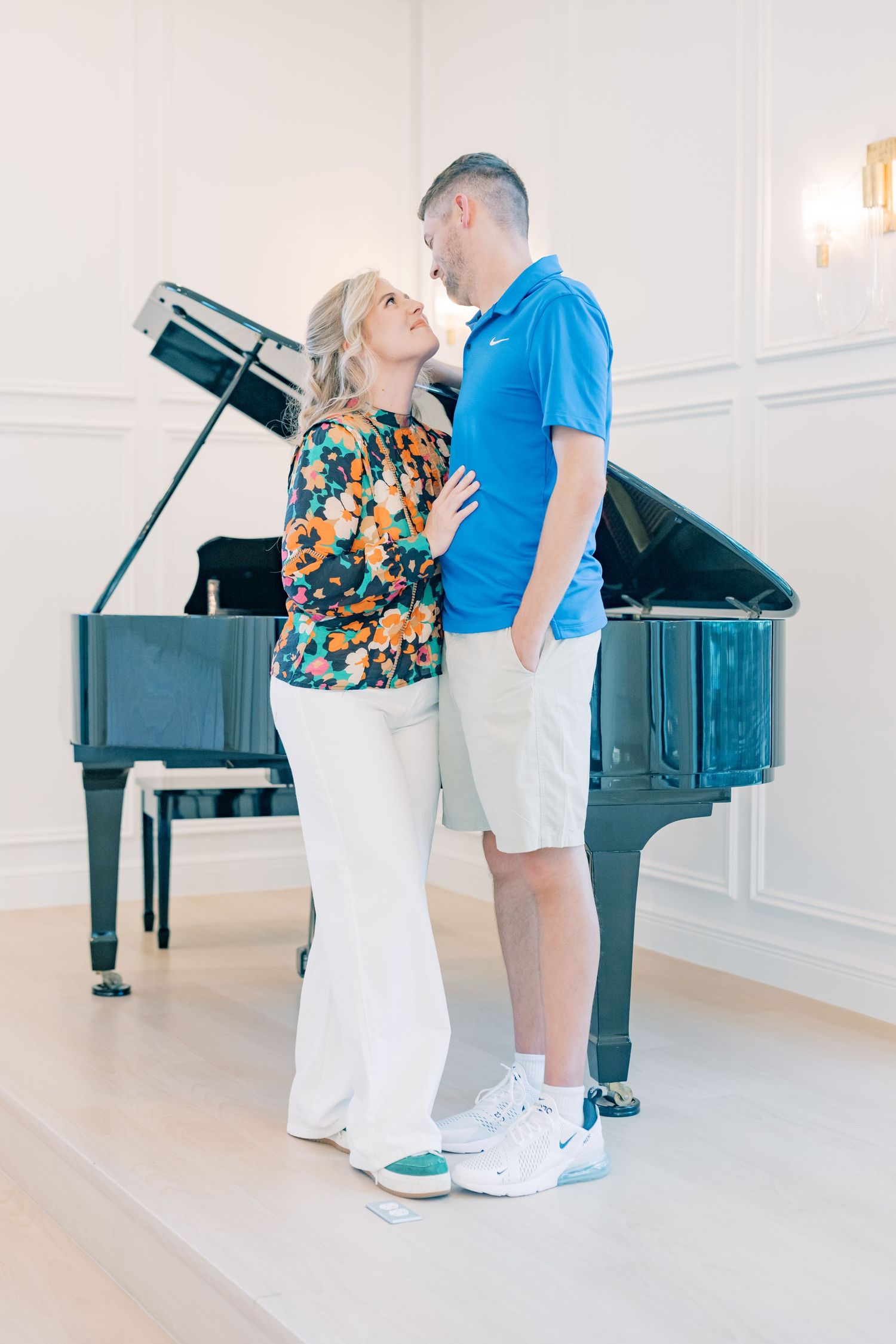 Couple gazing into each other eyes standing before an open grand piano in an elegant white room.