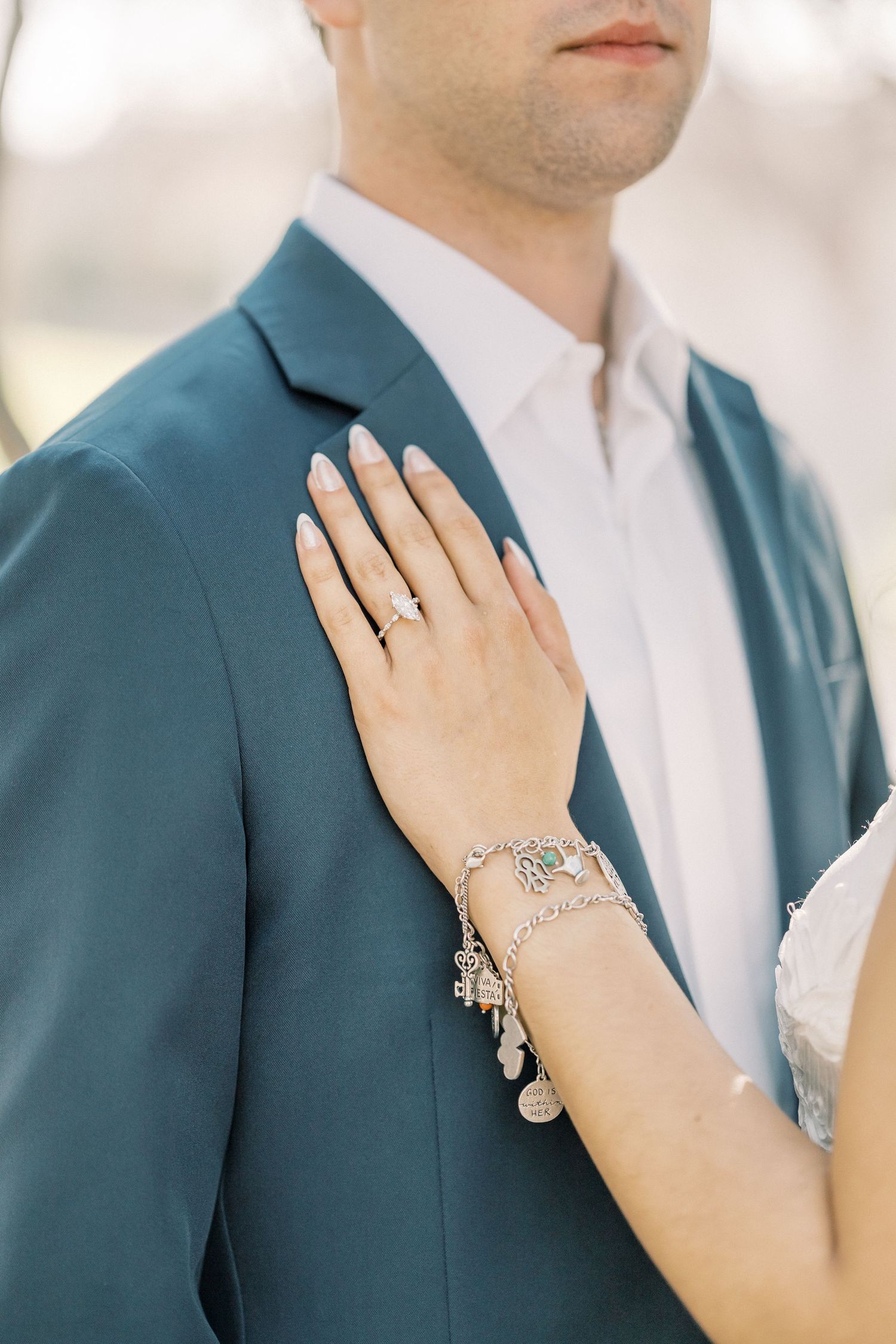 Close-up view of a couple in formal attire showing an engagement ring and teal suit jacket.