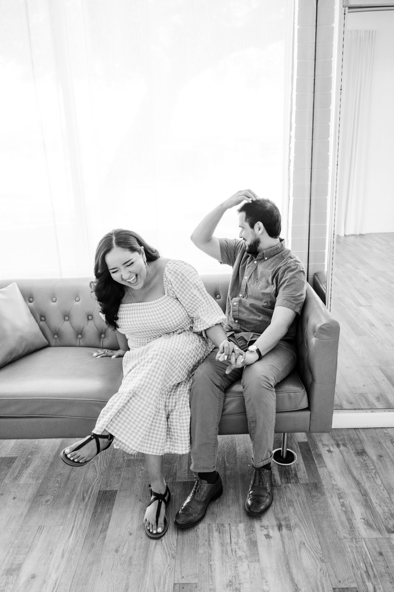 A joyful couple sharing a laugh while relaxing on a brown leather couch.