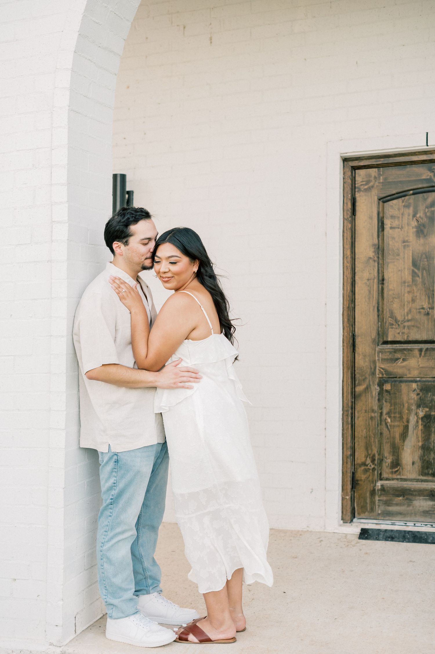 A romantic embrace between two people in light summer clothing against a rustic Mediterranean backdrop.
