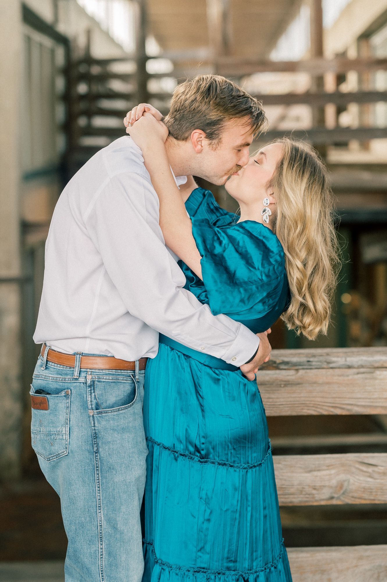 An intimate moment shared between a couple on wooden stairs, she in teal and he in white and denim.