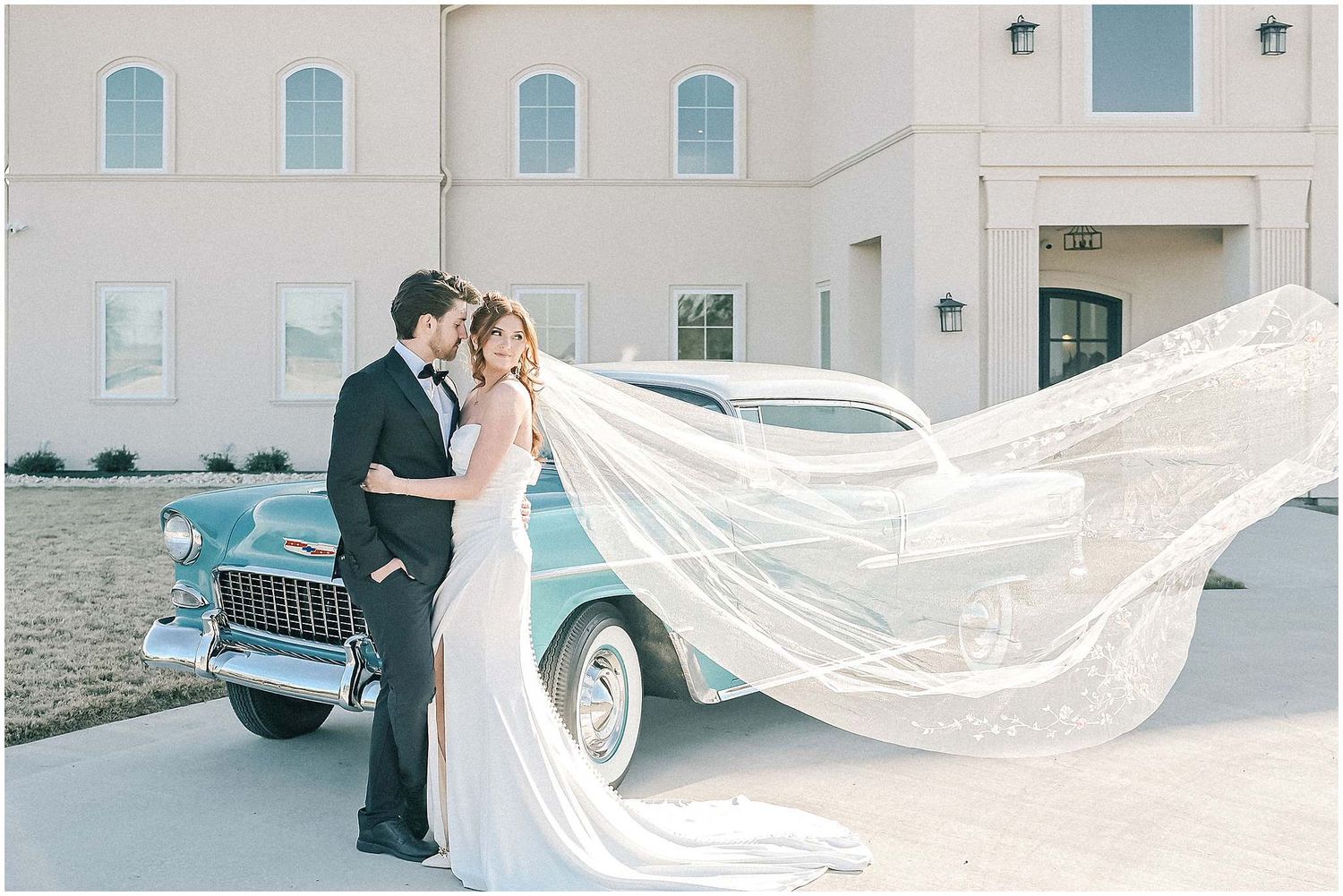 Dramatic wedding veil flowing in the wind outside a light-colored building.