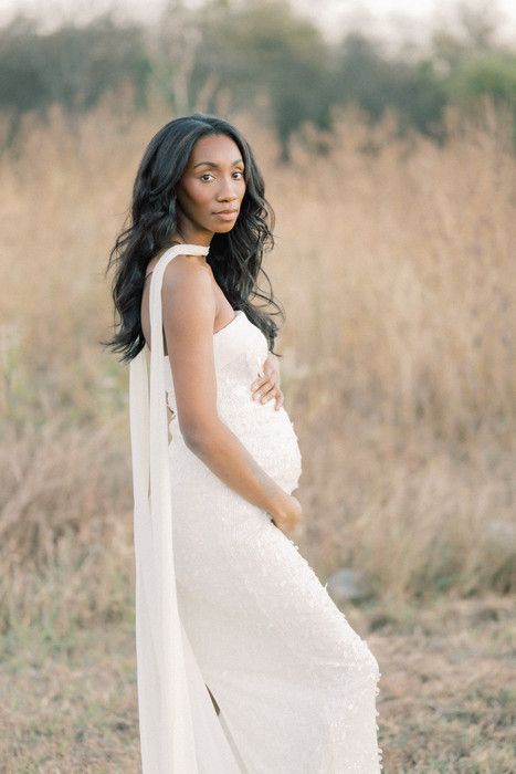 Elegant maternity session showcasing white lace gown in rustic outdoor setting.