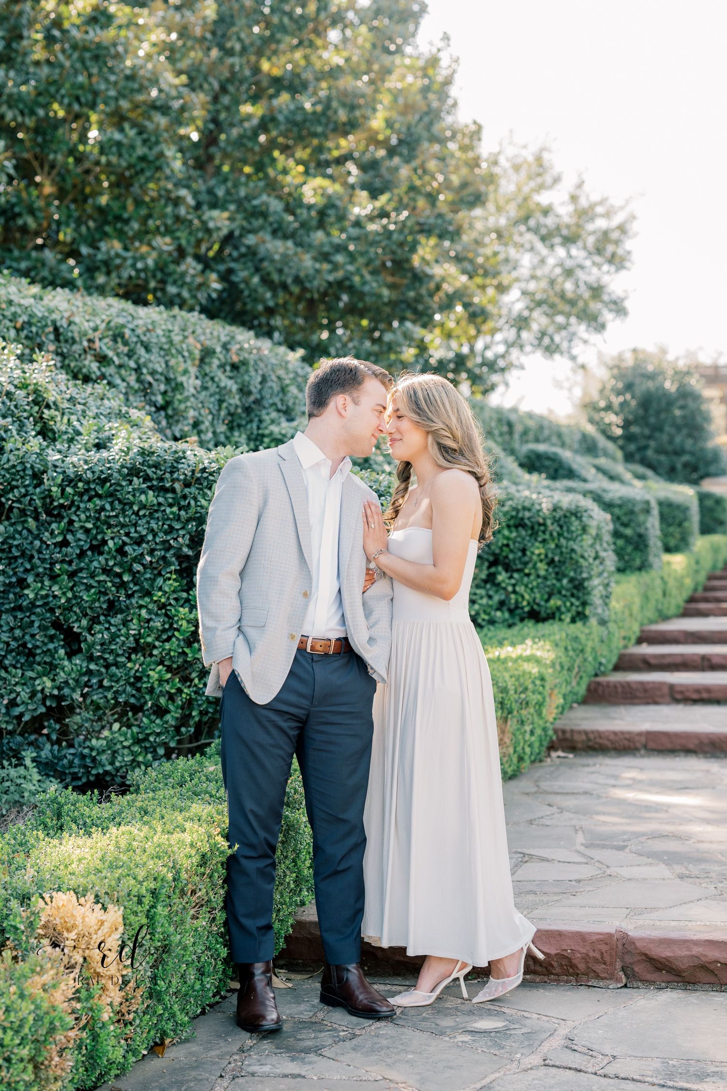 Couple shares intimate moments in a garden setting with stone steps and lush greenery in a series of romantic photos.