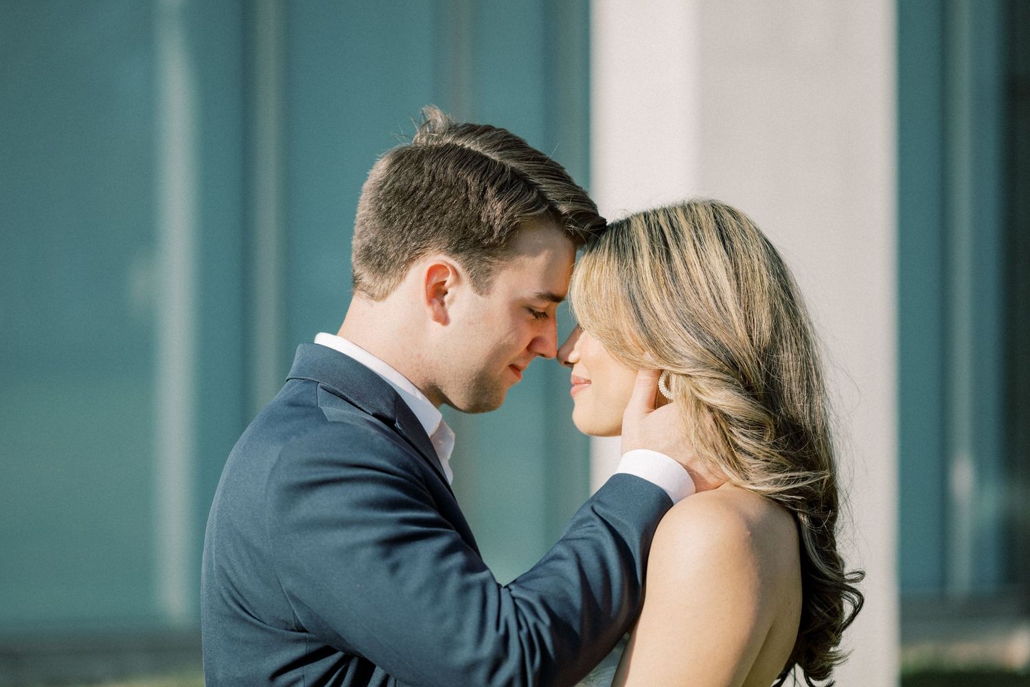A couple in formal wedding attire sharing an intimate kiss against a modern architectural backdrop.