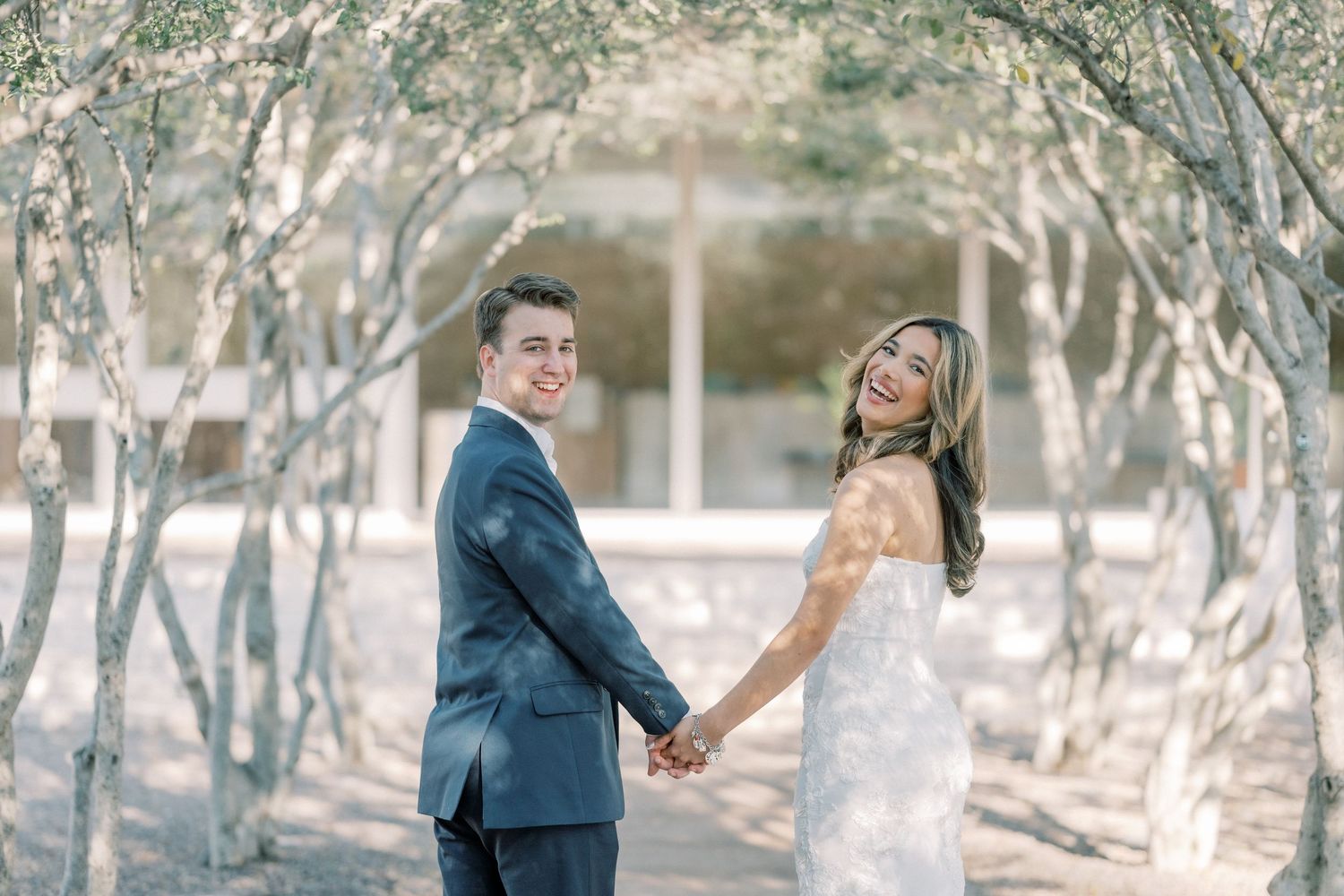 A couple walks hand in hand through a wooded outdoor setting during a romantic photo session.