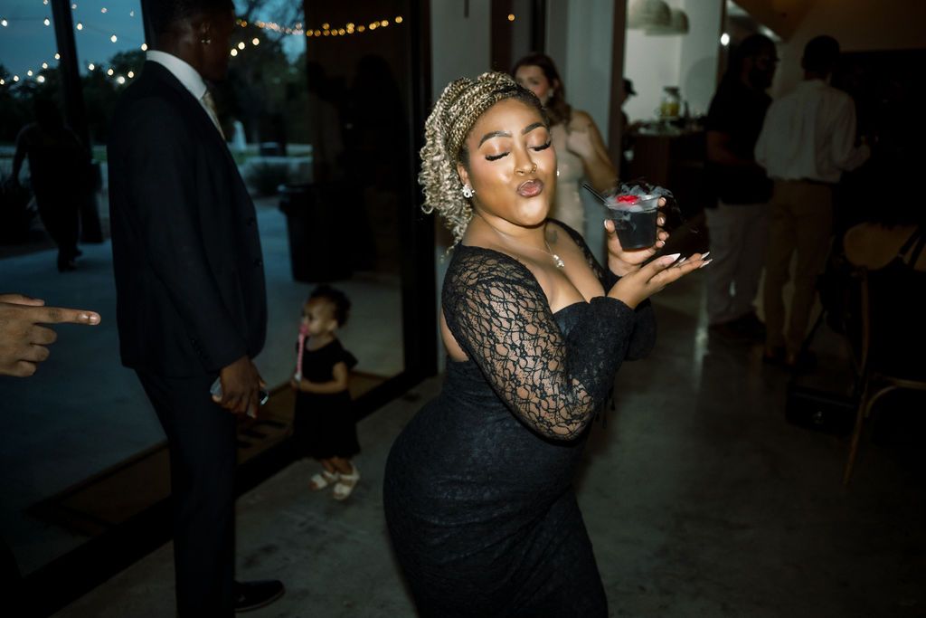 Woman in black lace dress posing playfully at an indoor evening party event.