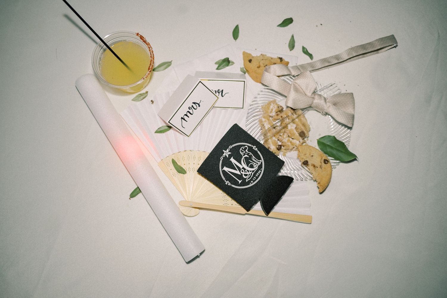 Wedding table setting with cocktail, menu cards, monogram koozie, and decorative greenery accents.