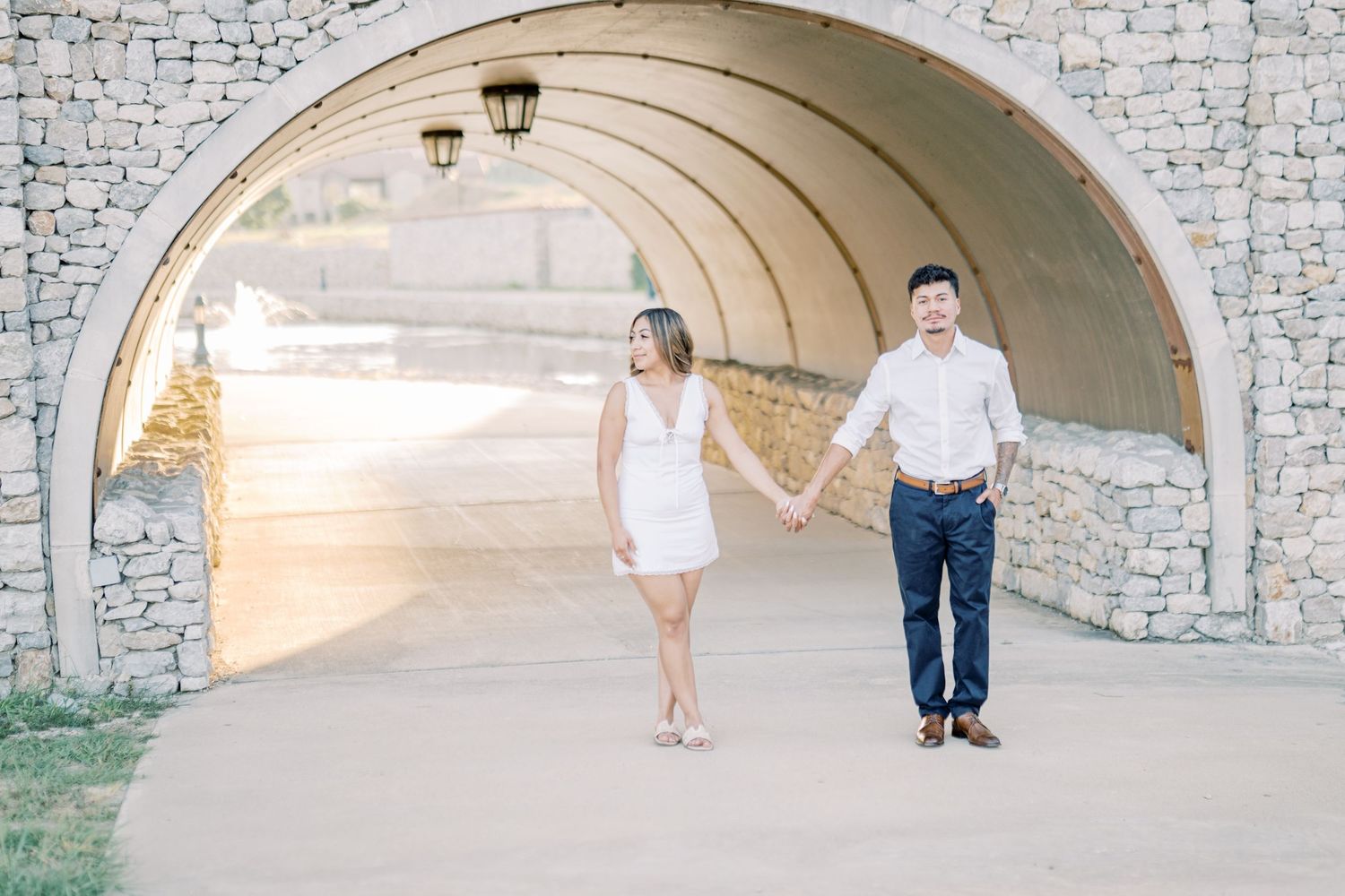 Couple holding hands walking through a stone archway tunnel during an engagement photo session.