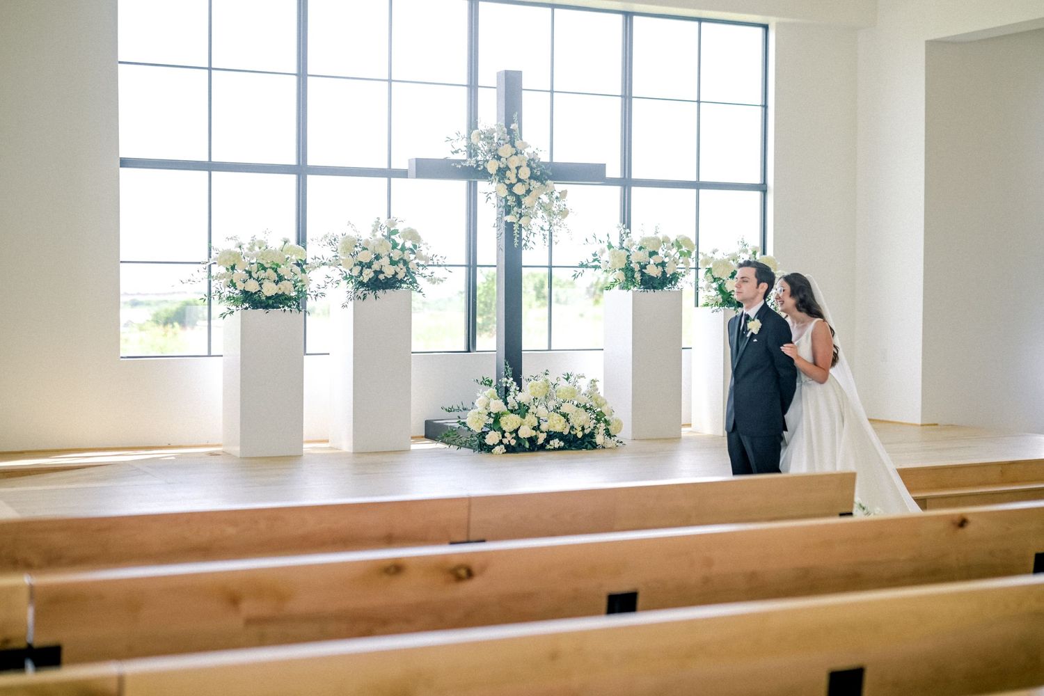 Bride and groom sharing a kiss at the altar adorned with white floral arrangements and a cross.