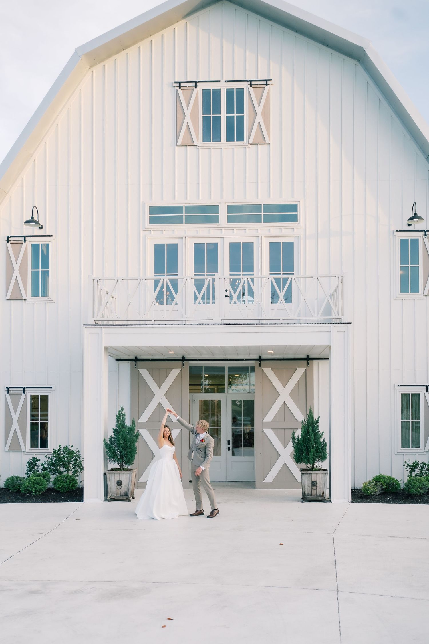 Bride and groom dancing in front of a white barn wedding venue with large sliding doors and balcony.