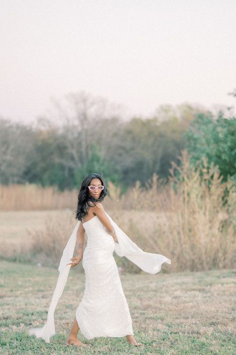 Ethereal maternity photo of a woman in white dress twirling with flowing fabric in a sunlit field.