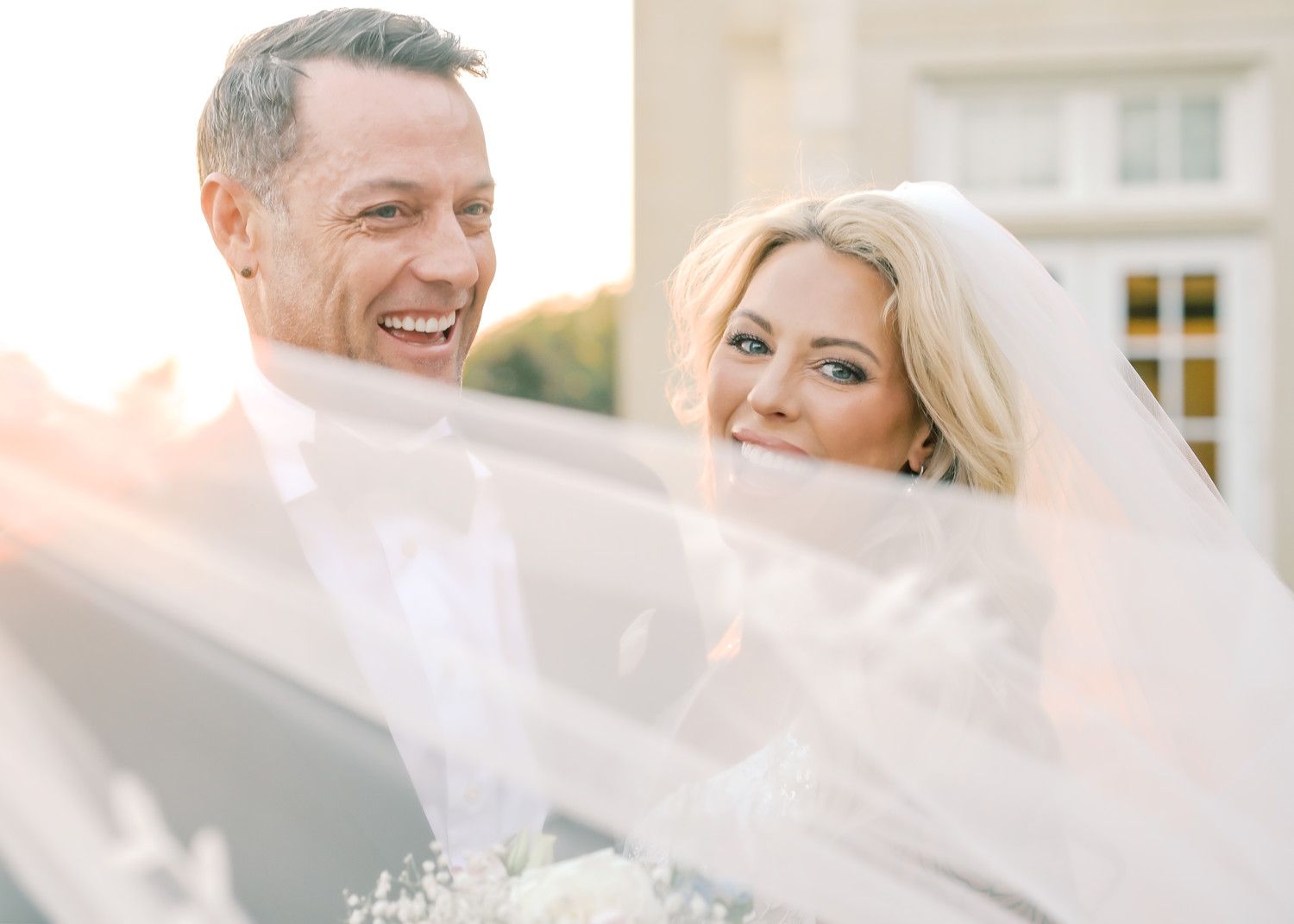 Sun-kissed wedding portrait showing happy couple through delicate veil.