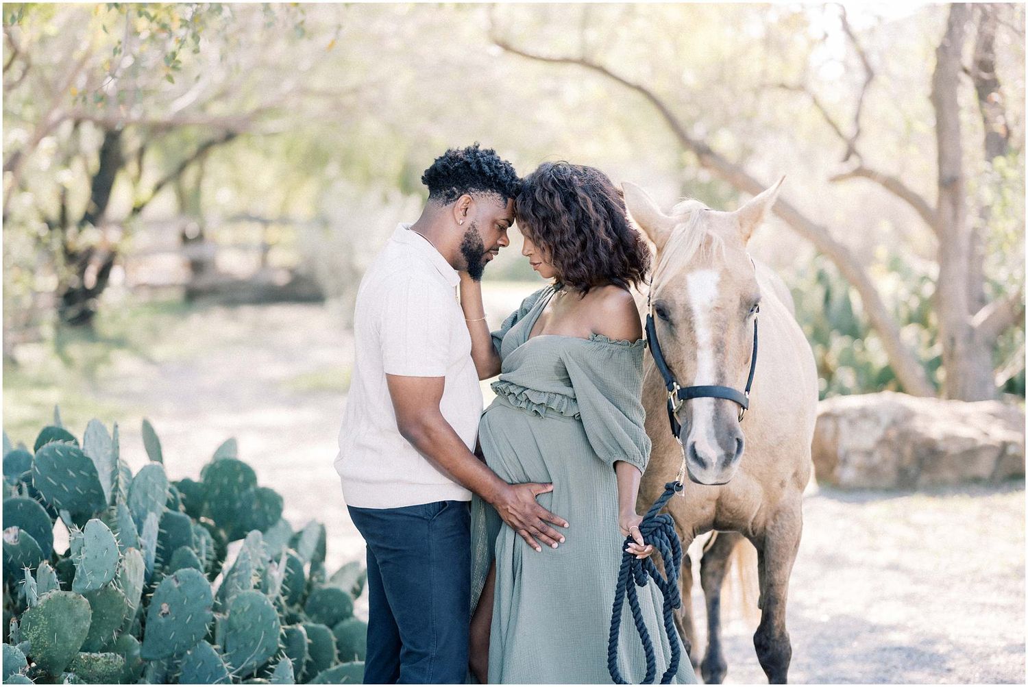 A couple poses together in a rustic outdoor setting with cactus plants and natural lighting.