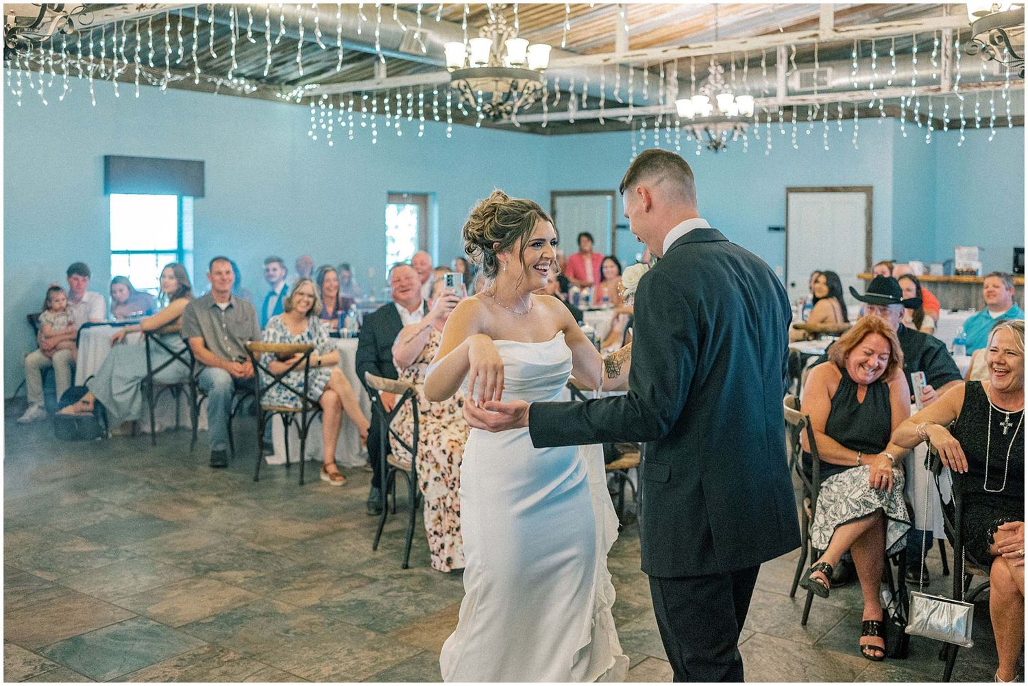 Reception hall with blue walls and hanging lights during wedding celebration.