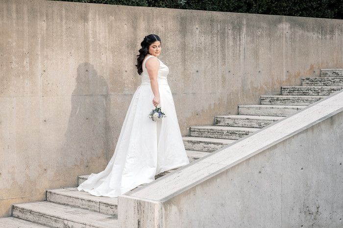 Bride in a white gown holding a bouquet poses gracefully on outdoor concrete steps.