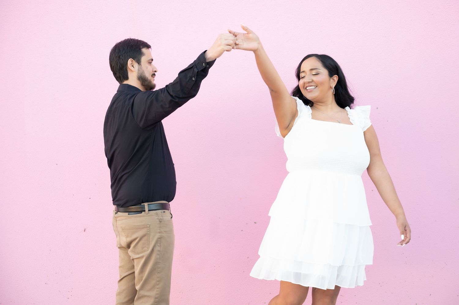 A dancing couple spins and laughs together against a pink backdrop.