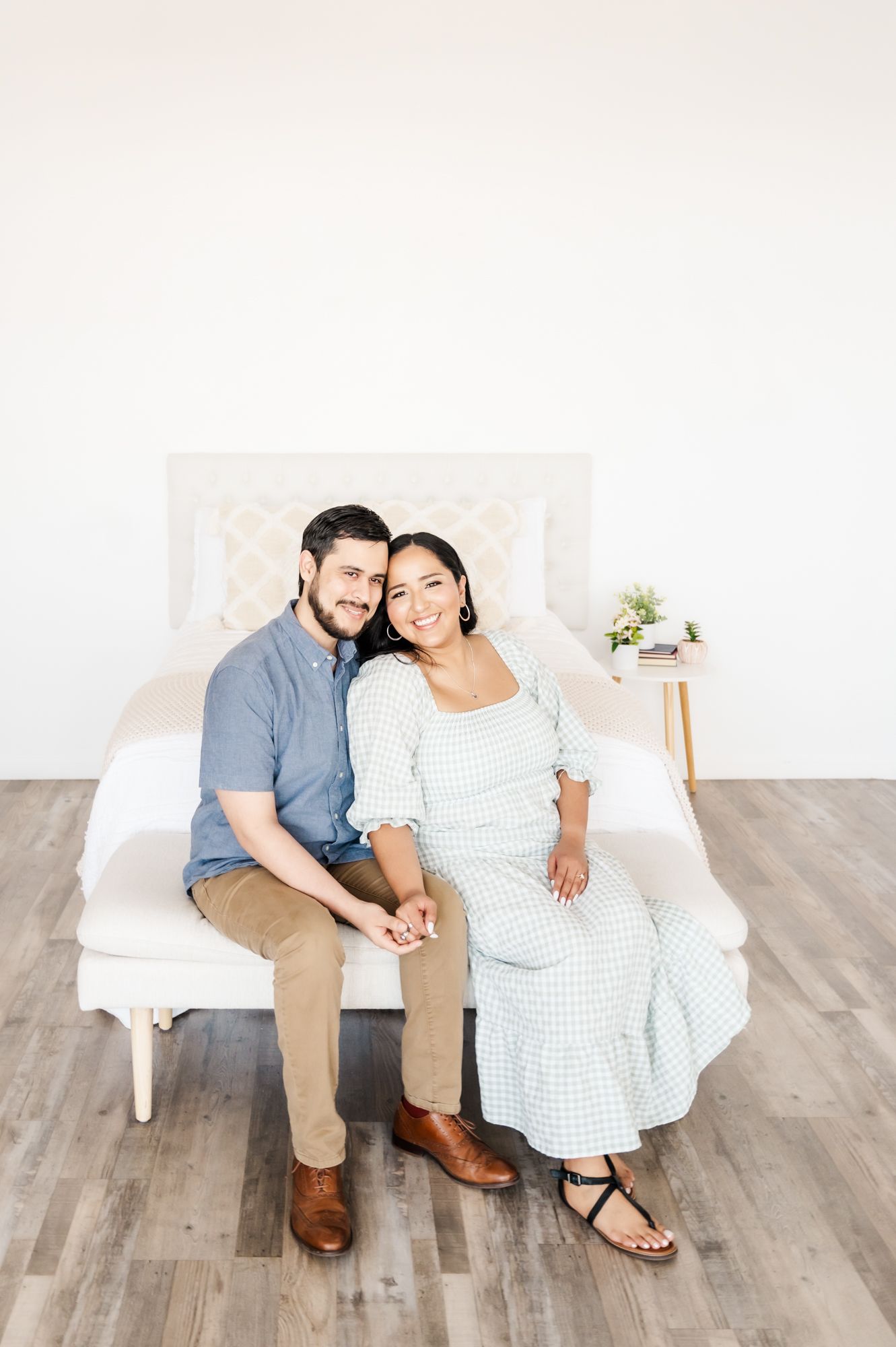A couple sits together on a white bench wearing coordinated casual outfits in a bright minimalist setting.