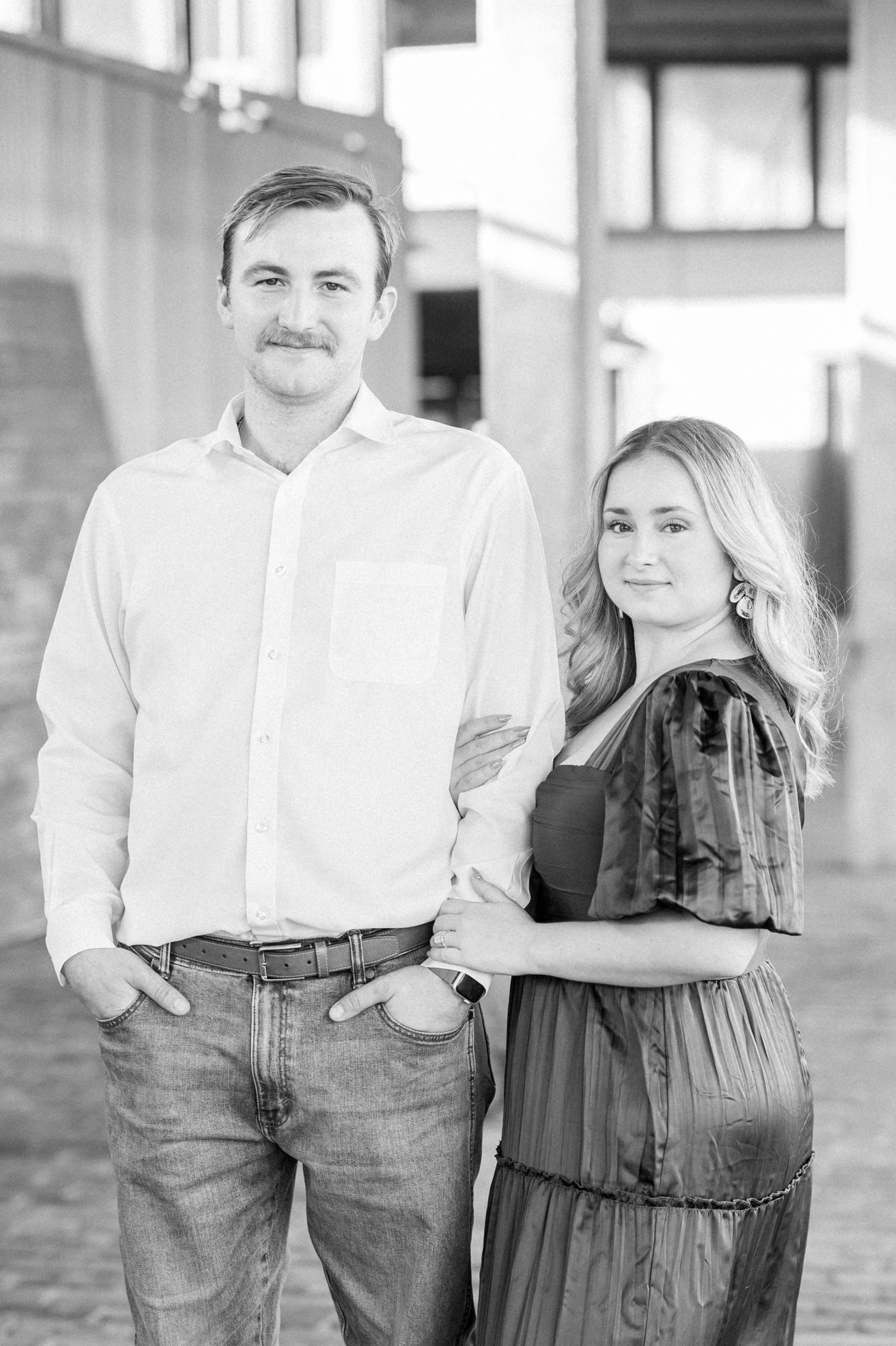 Black and white engagement photo series showing a couple in casual attire posing together on a city street.