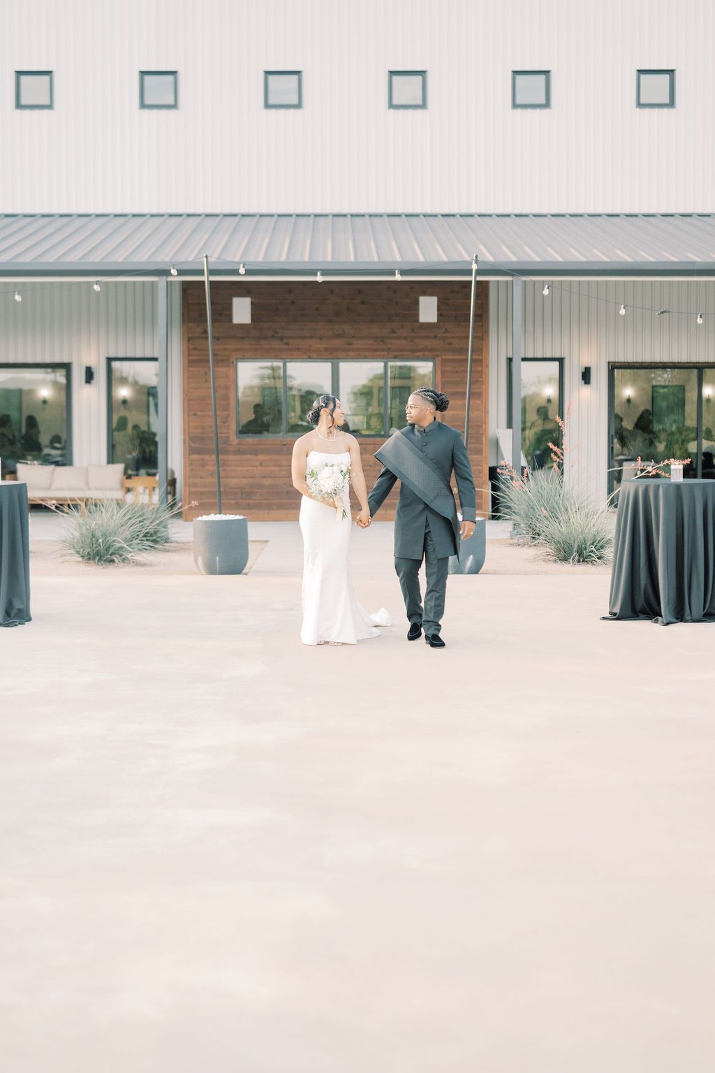 Bride and groom walking hand in hand outside a modern white barn wedding venue with wood accents and elegant decor.