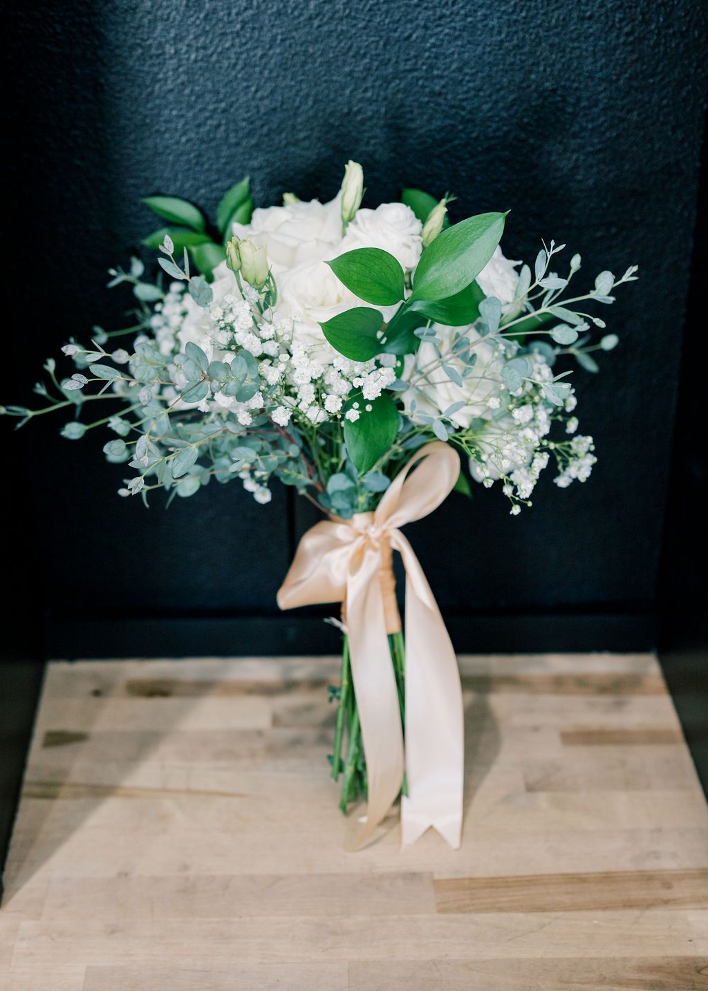 Elegant bridal bouquet with white roses, baby's breath, succulents, and greenery tied with a blush satin ribbon.