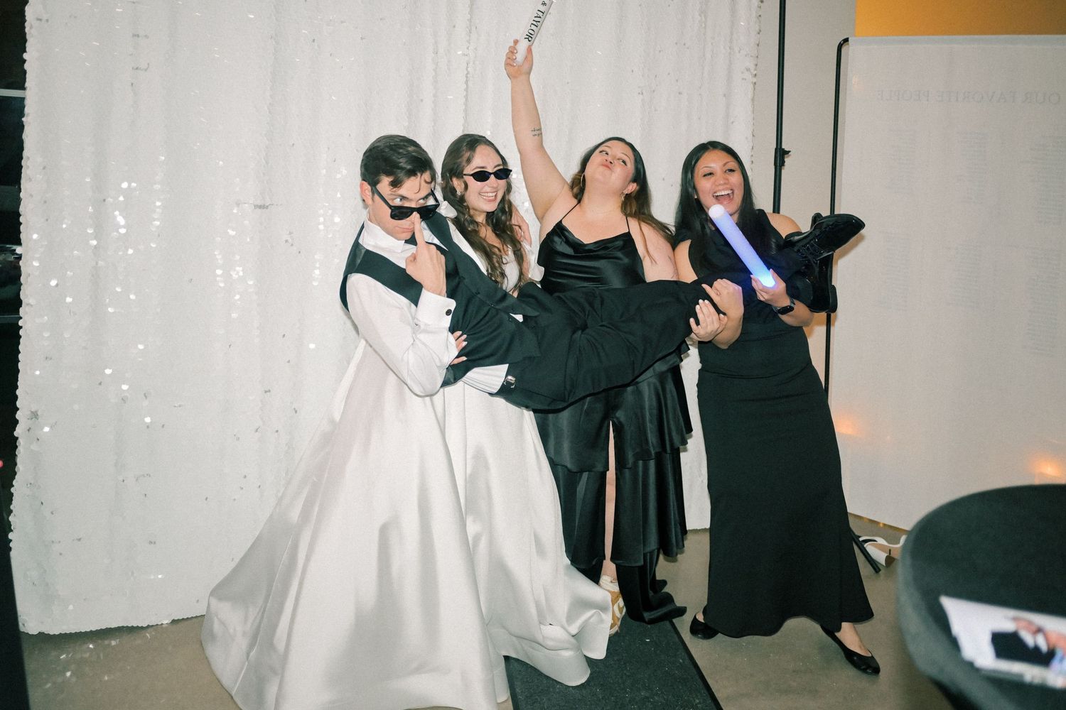 Bride and bridesmaids in black dresses posing and dancing at wedding photo booth.