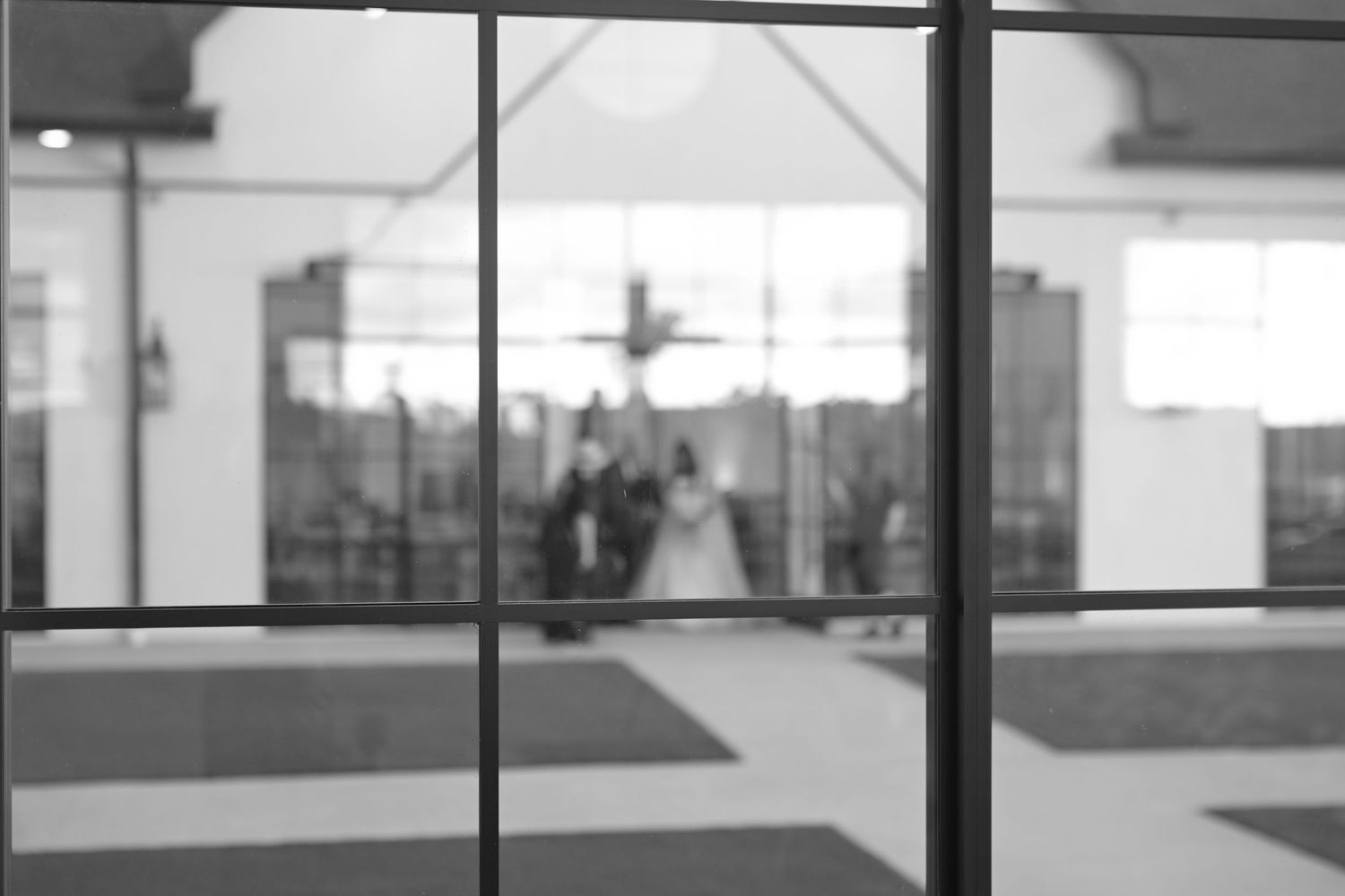 Black and white photo of bride and groom reflected through glass doors at wedding venue.