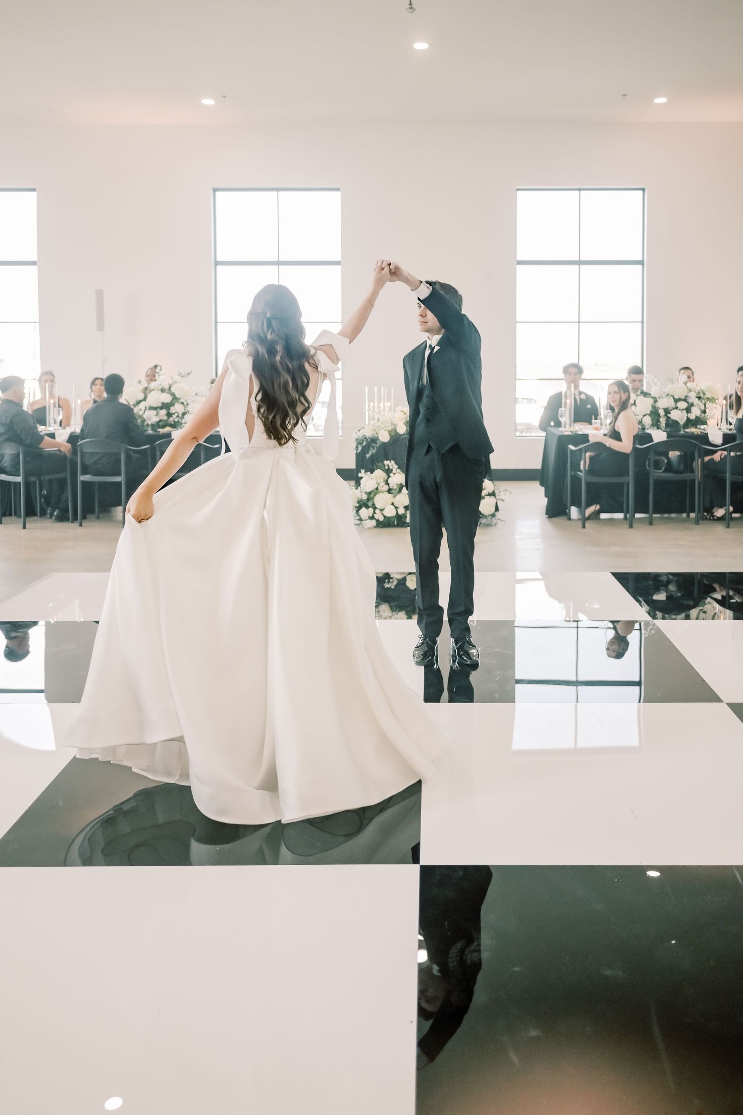 Bride and groom sharing first dance on a black and white checkered floor at their wedding reception.