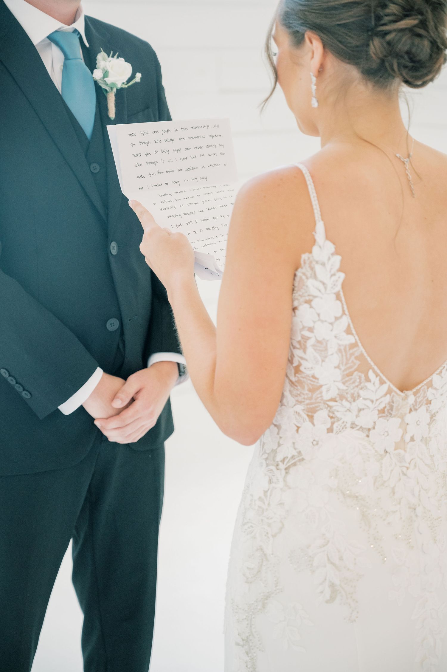Close-up details of a couple's first look moment showing lace wedding dress and dark suit.
