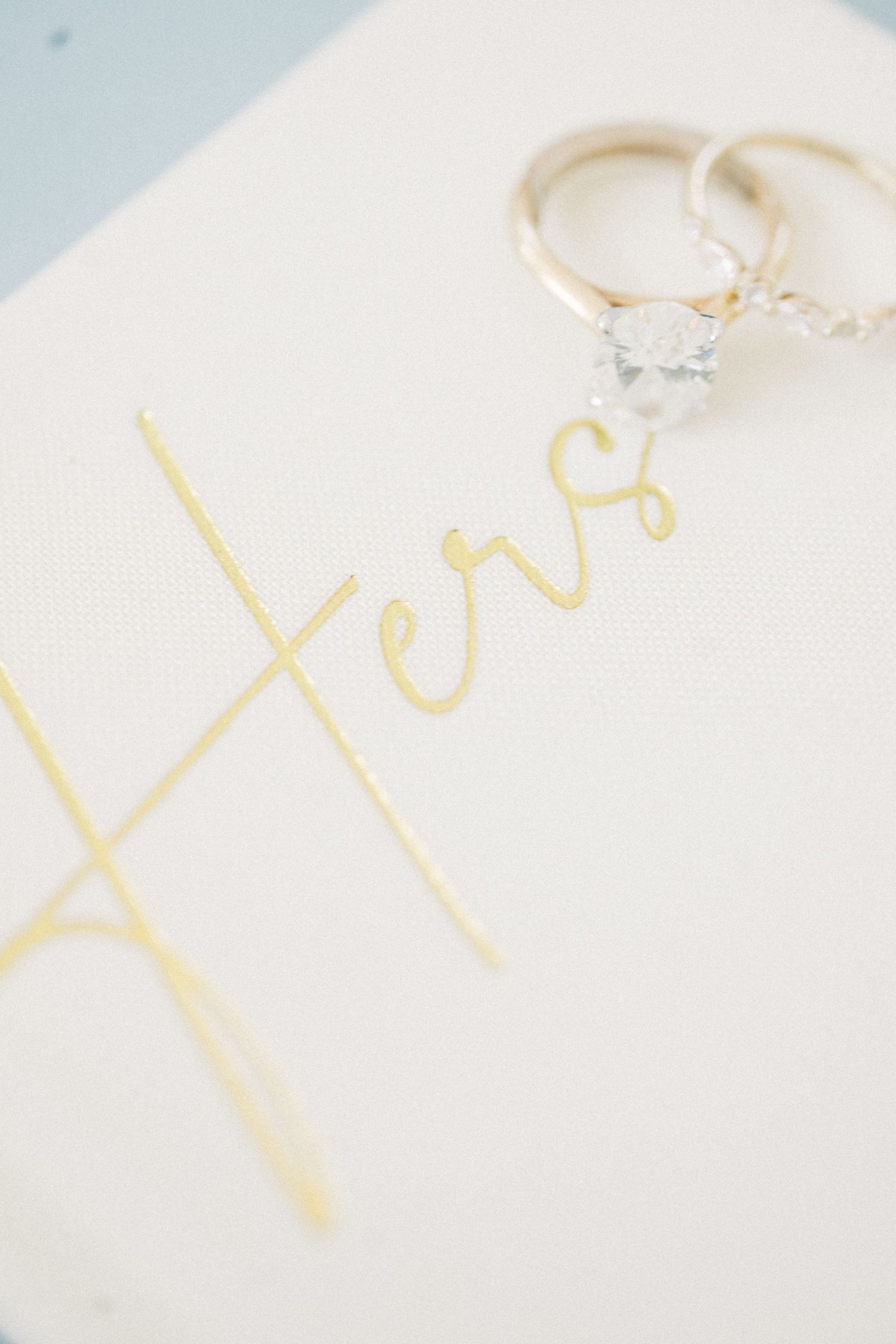 Two wedding rings resting on a white card with gold script reading Hers, elegant bridal jewelry detail photo.