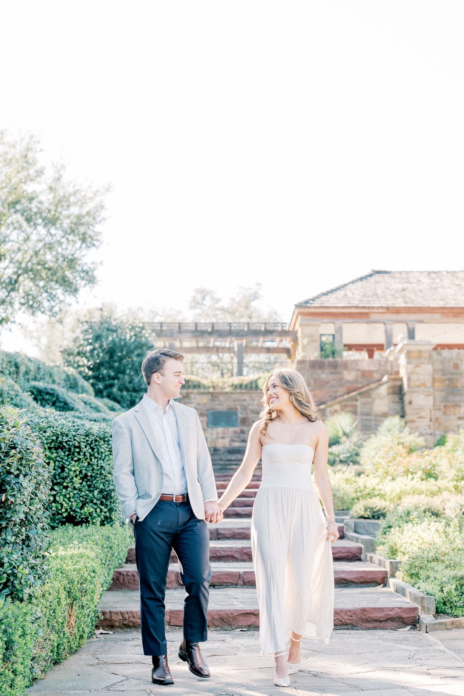A couple shares a joyful moment together while walking along brick steps in a sunny garden setting.