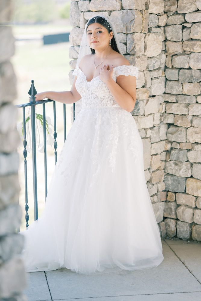 Full-length bridal portrait showcasing off-shoulder wedding gown against stone archway.