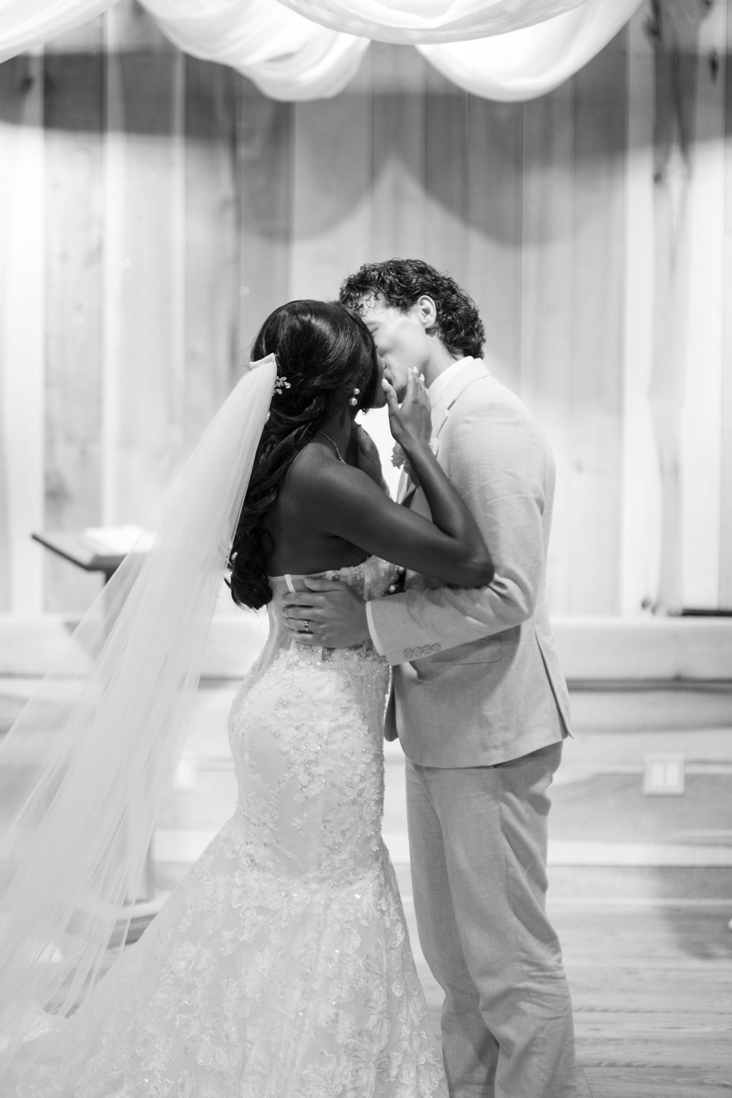 Black and white photo of a bride and groom sharing their first kiss at the altar during their wedding ceremony.