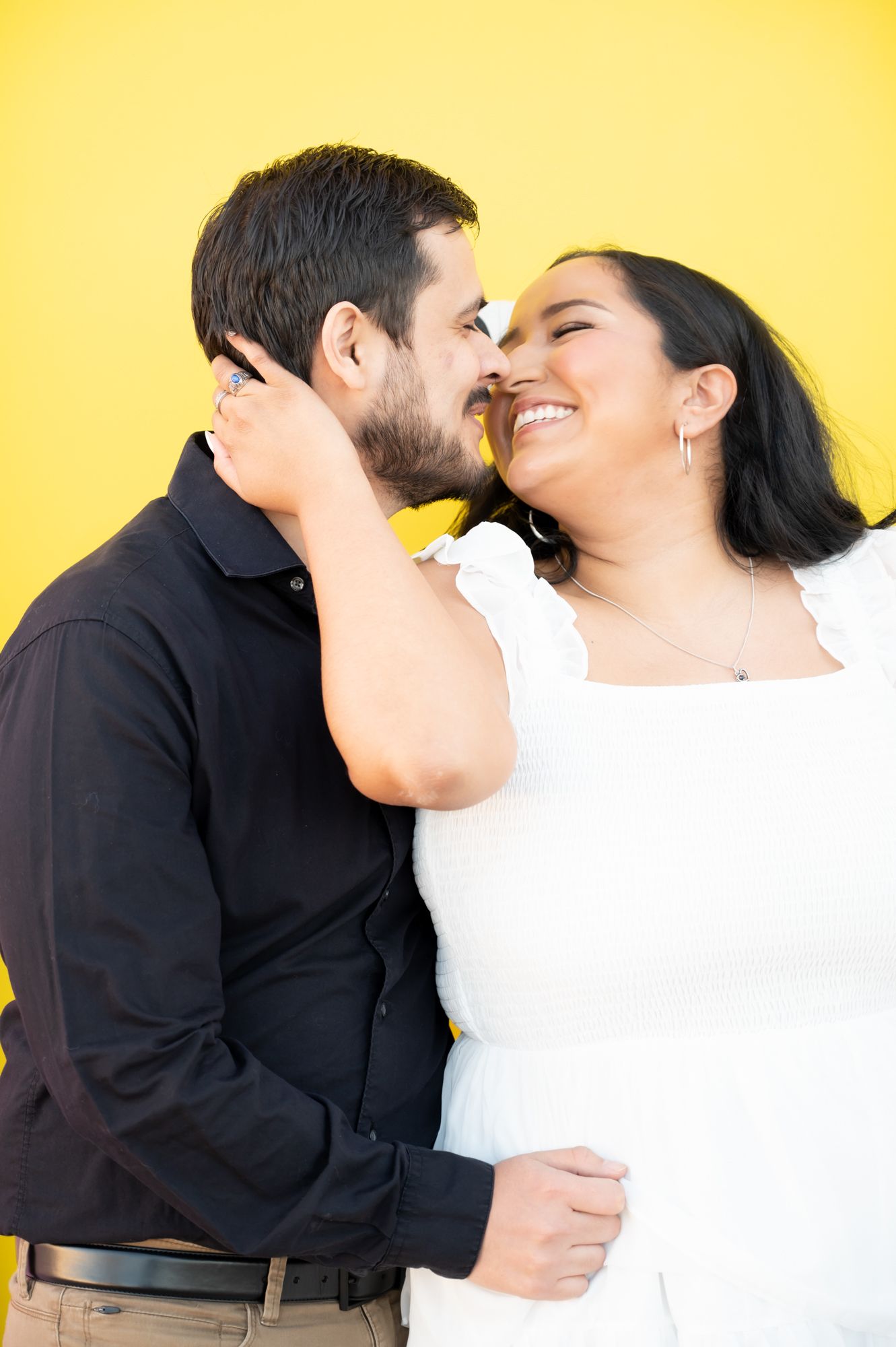 A tender moment captured between a couple against a vibrant yellow wall.
