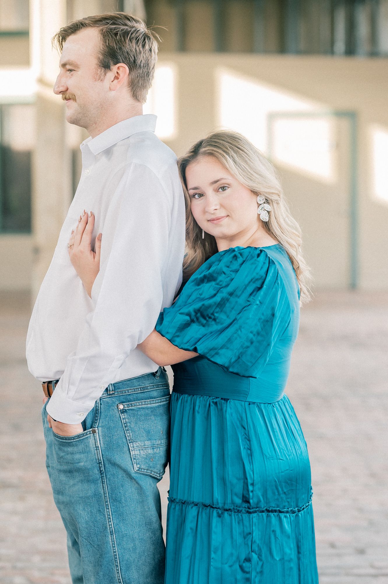 Romantic couple poses together in an industrial space with natural lighting.