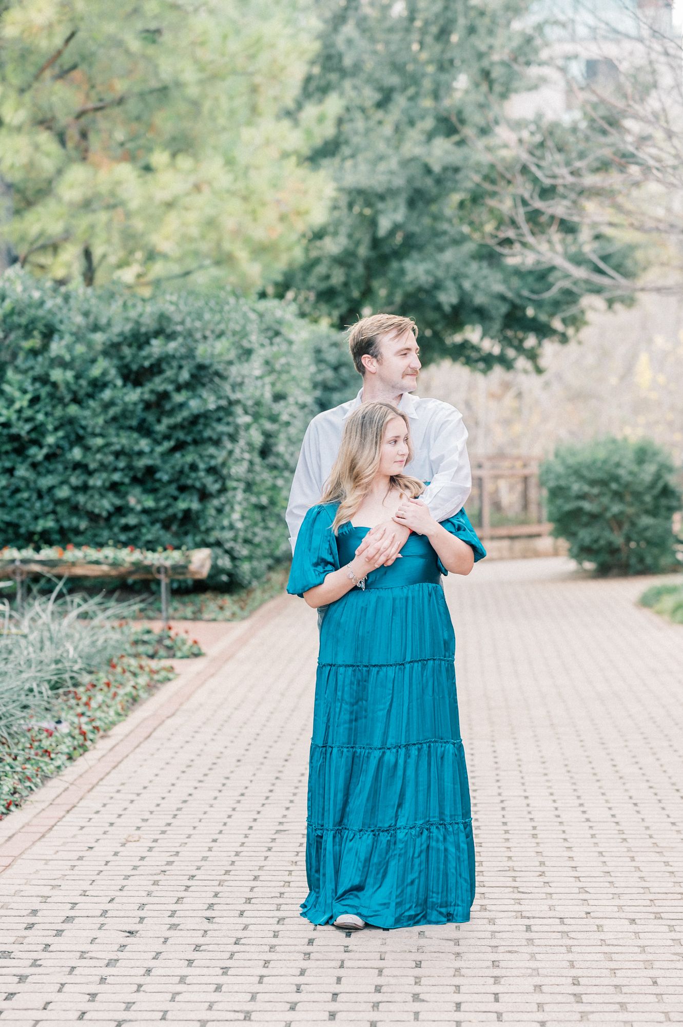 A couple shares a tender moment on a brick paved pathway surrounded by lush garden greenery.